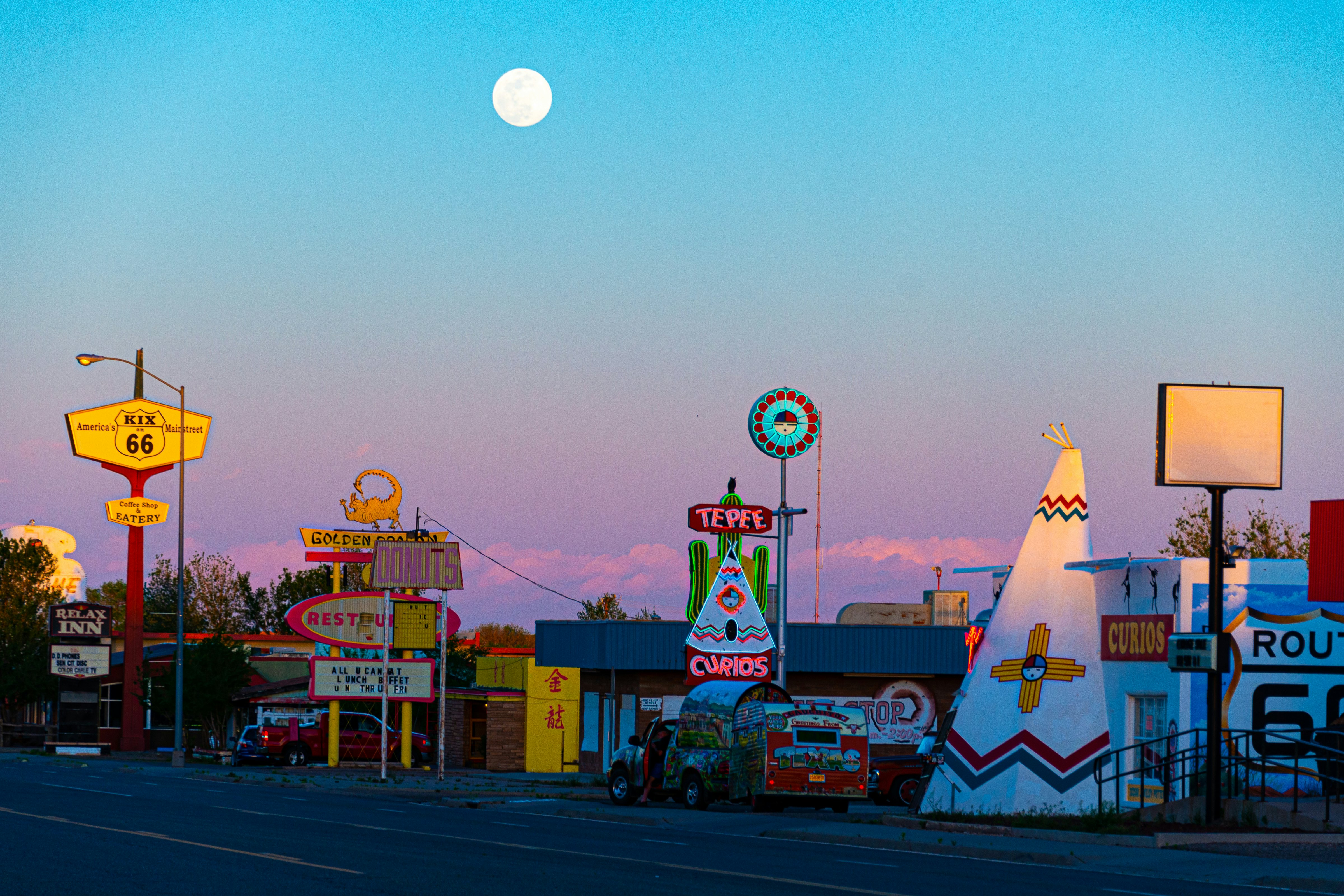 Roadside hotels, restaurants and stores lit up in neon under a full moon.