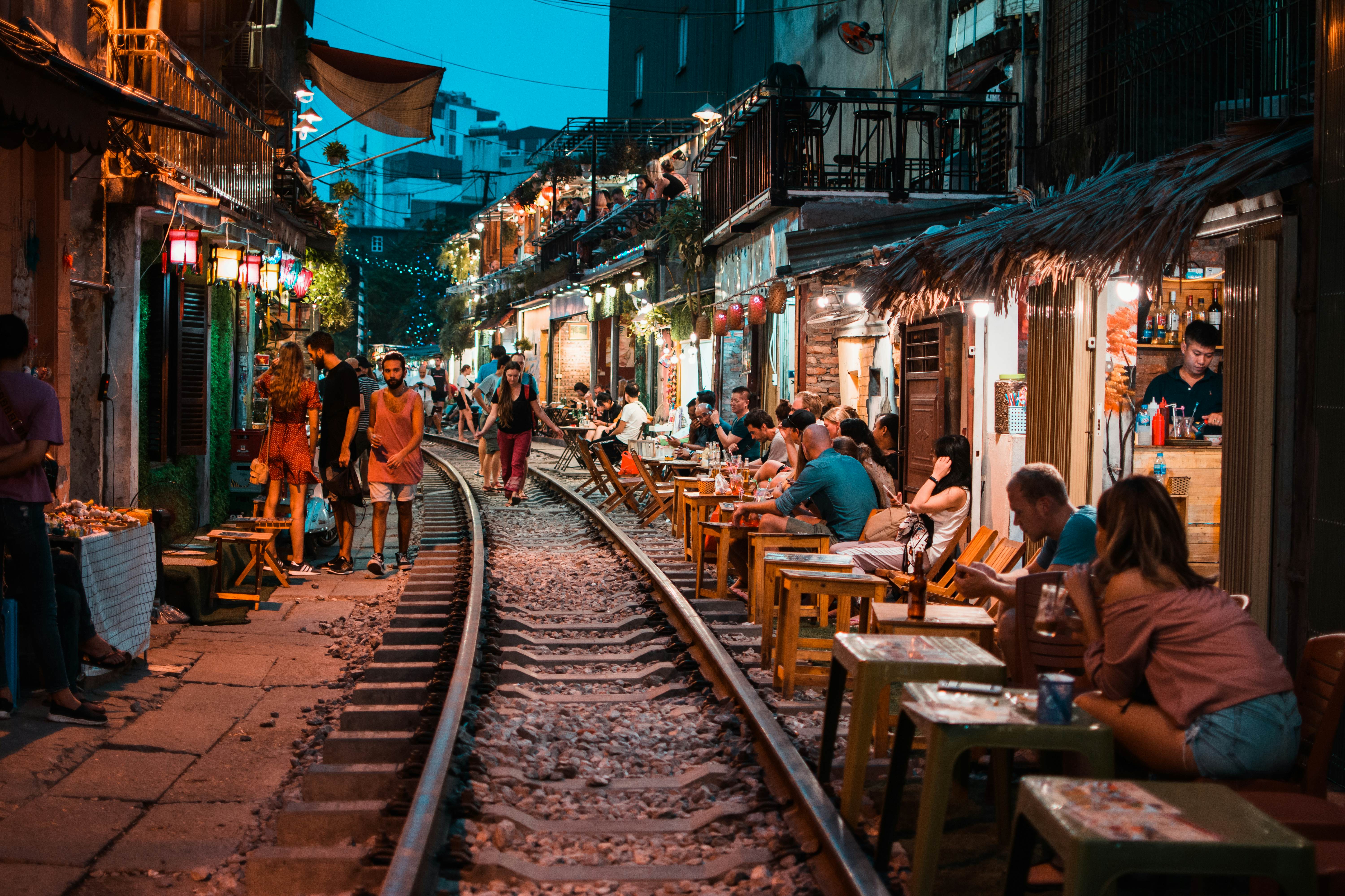 Train tracks run through an alley flanked by restaurants and small tables