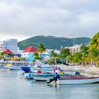 Philipsburg, Sint Maarten. Boats docked on tropical Caribbean island coast with white sand and coconut palm trees. Tourists & locals shop at stores and restaurants on shore. Mountain landscape behind., License Type: media, Download Time: 2025-11-24T15:28:42.000Z, User: Malecia.Elamin_Lonelyplanet, Editorial: false, purchase_order: 65050 - Digital Destinations and Articles, job: Online editorial, client: A guide to Sint Maarten, other: Malecia Walker