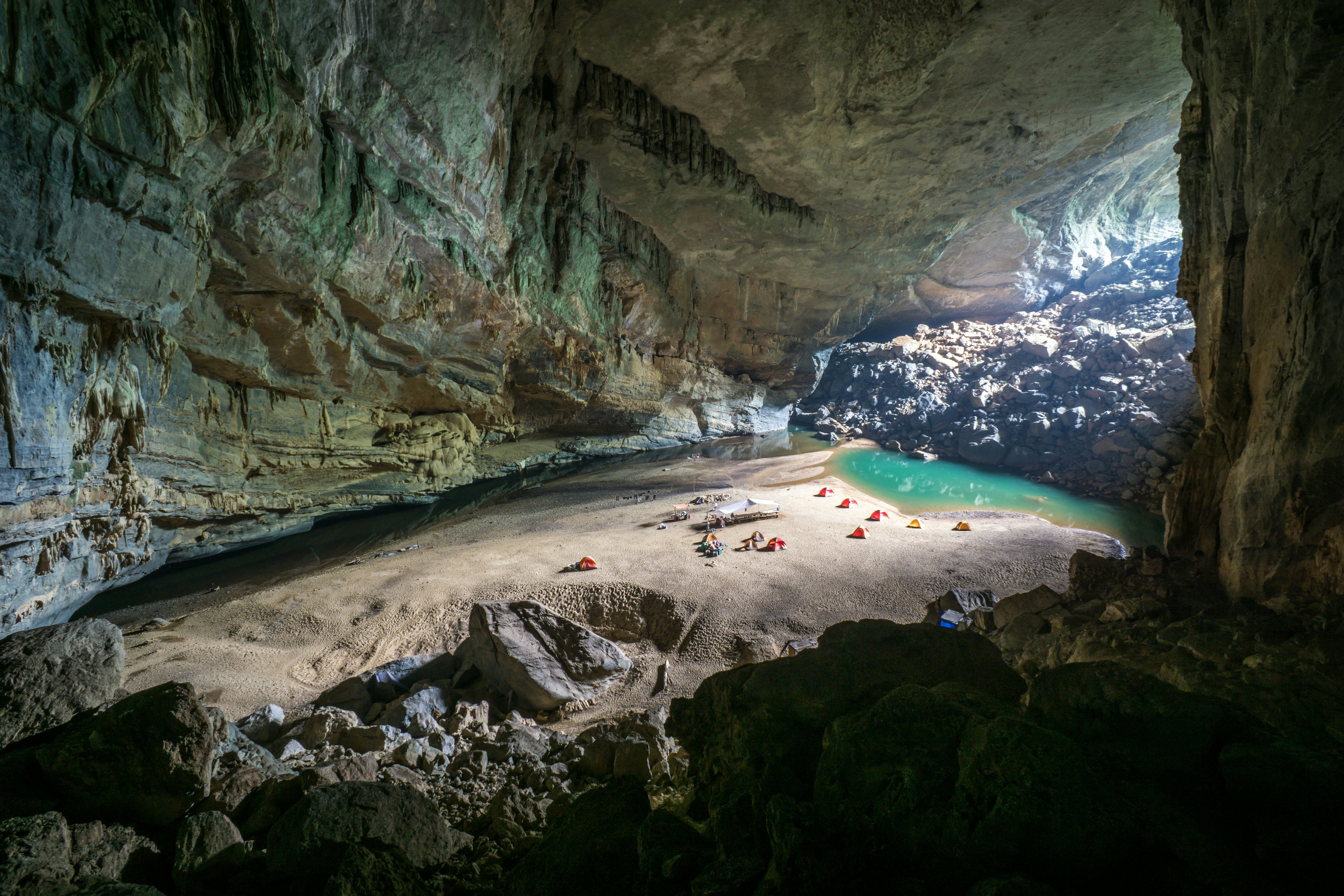 A wide shot of tents pitched on a beach in a huge underground cavern.