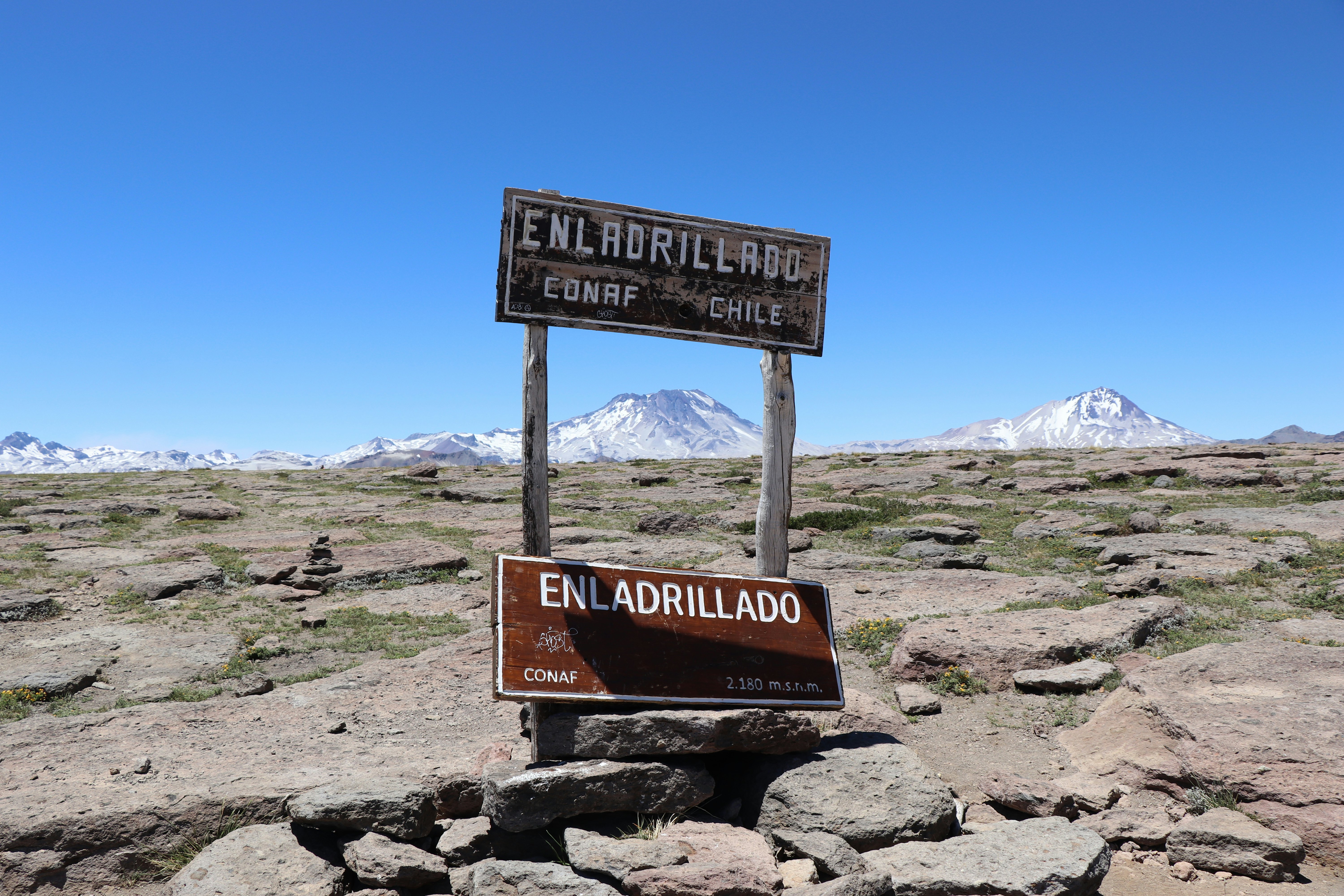 A sign on a high-altitude plateau of basalt rocks with mountains in the distance.