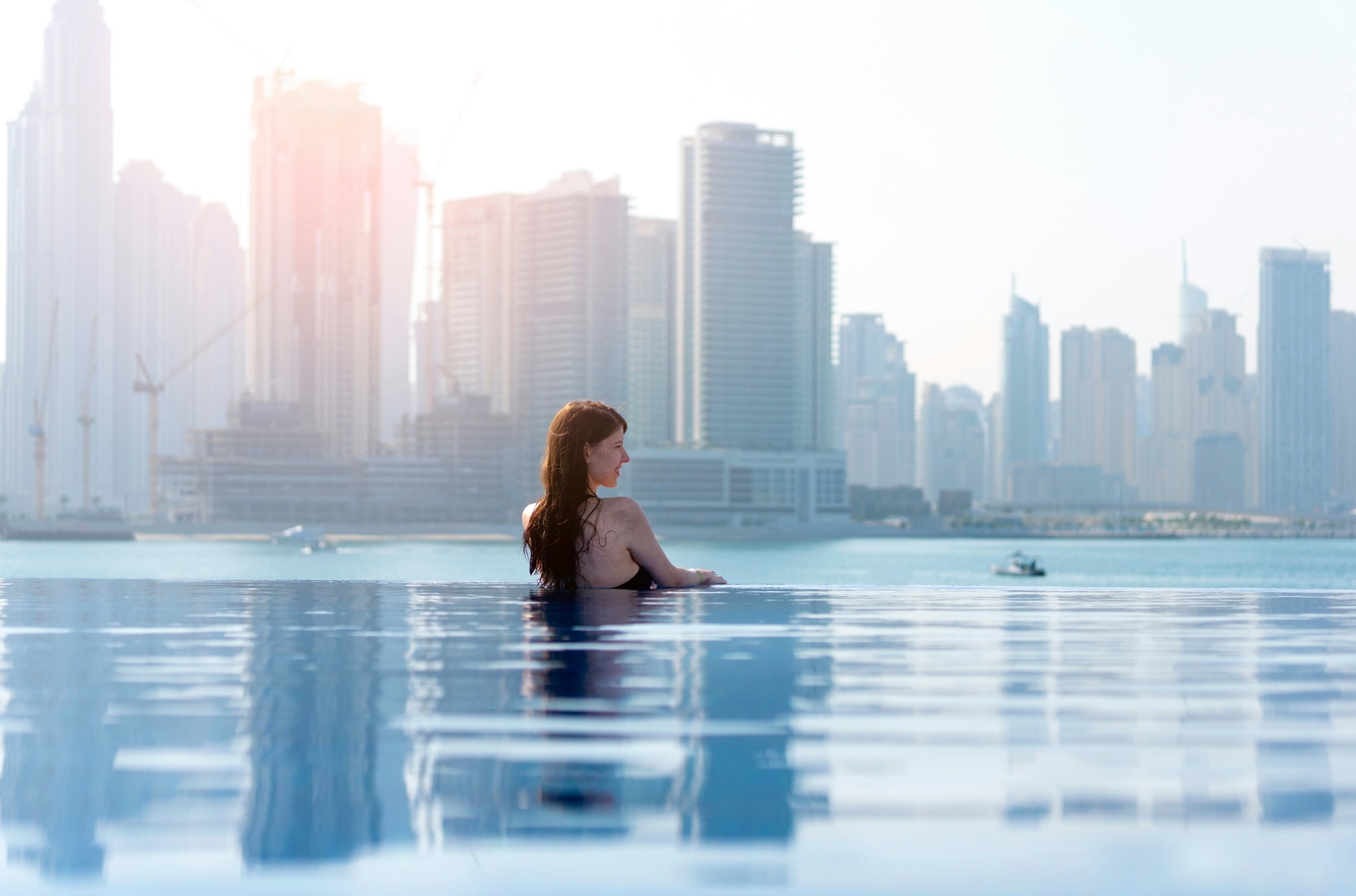 A woman is pictured in an infinity pool, with the skyline of a city behind her, across a bay.