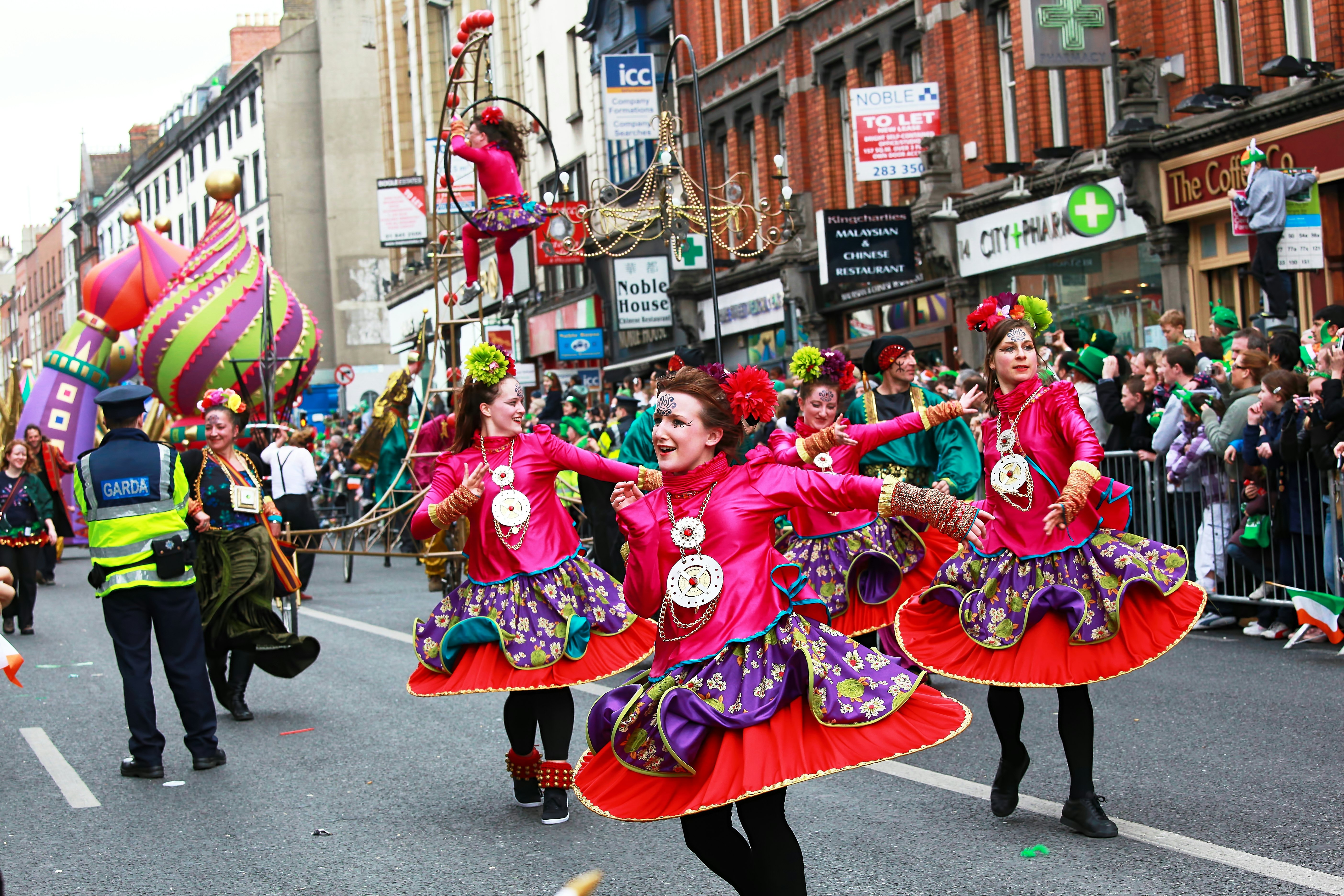 Women in red dresses twirl their hems while dancing in a parade on an overcast day.