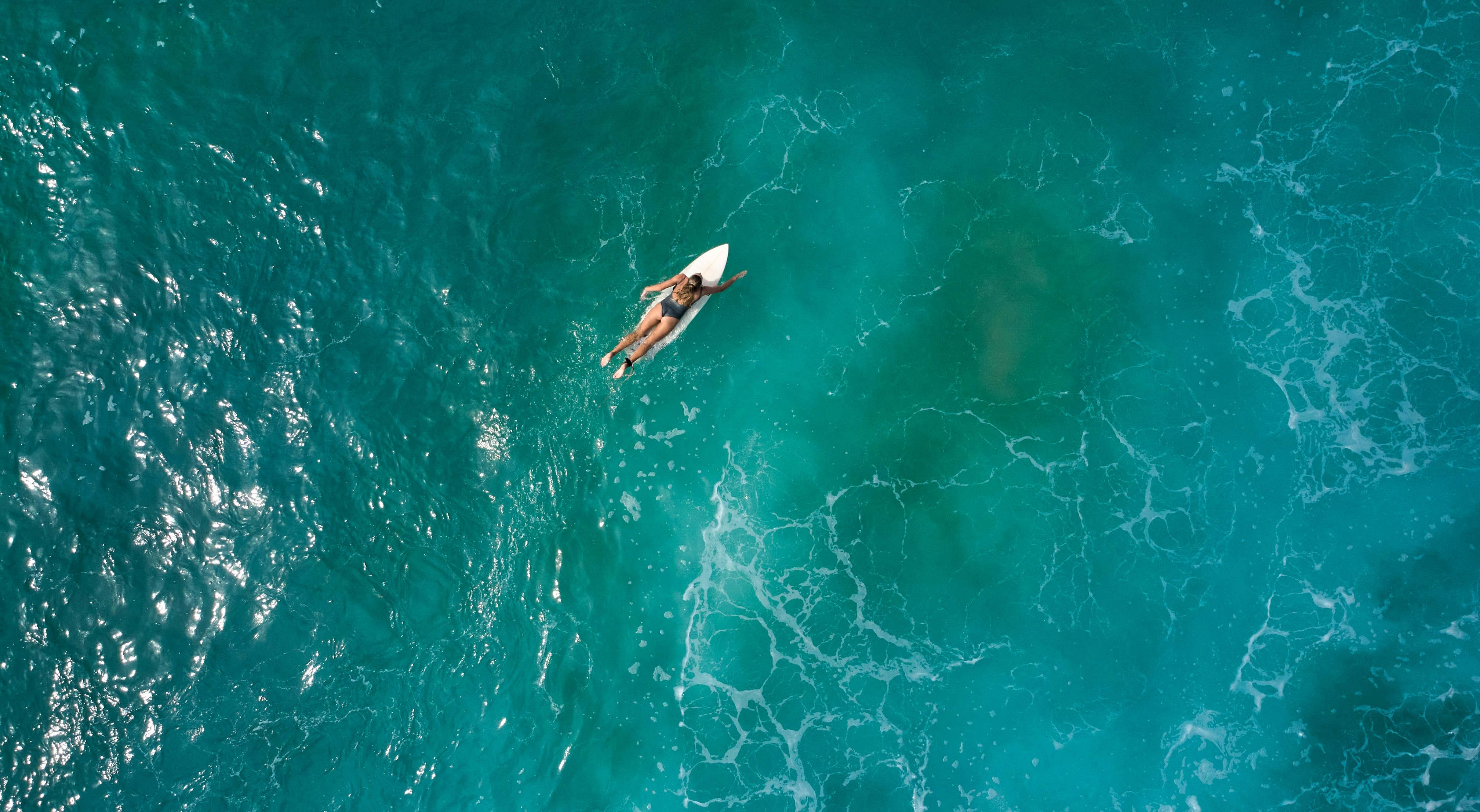 A surfer in the ocean paddles along on her surfboard.