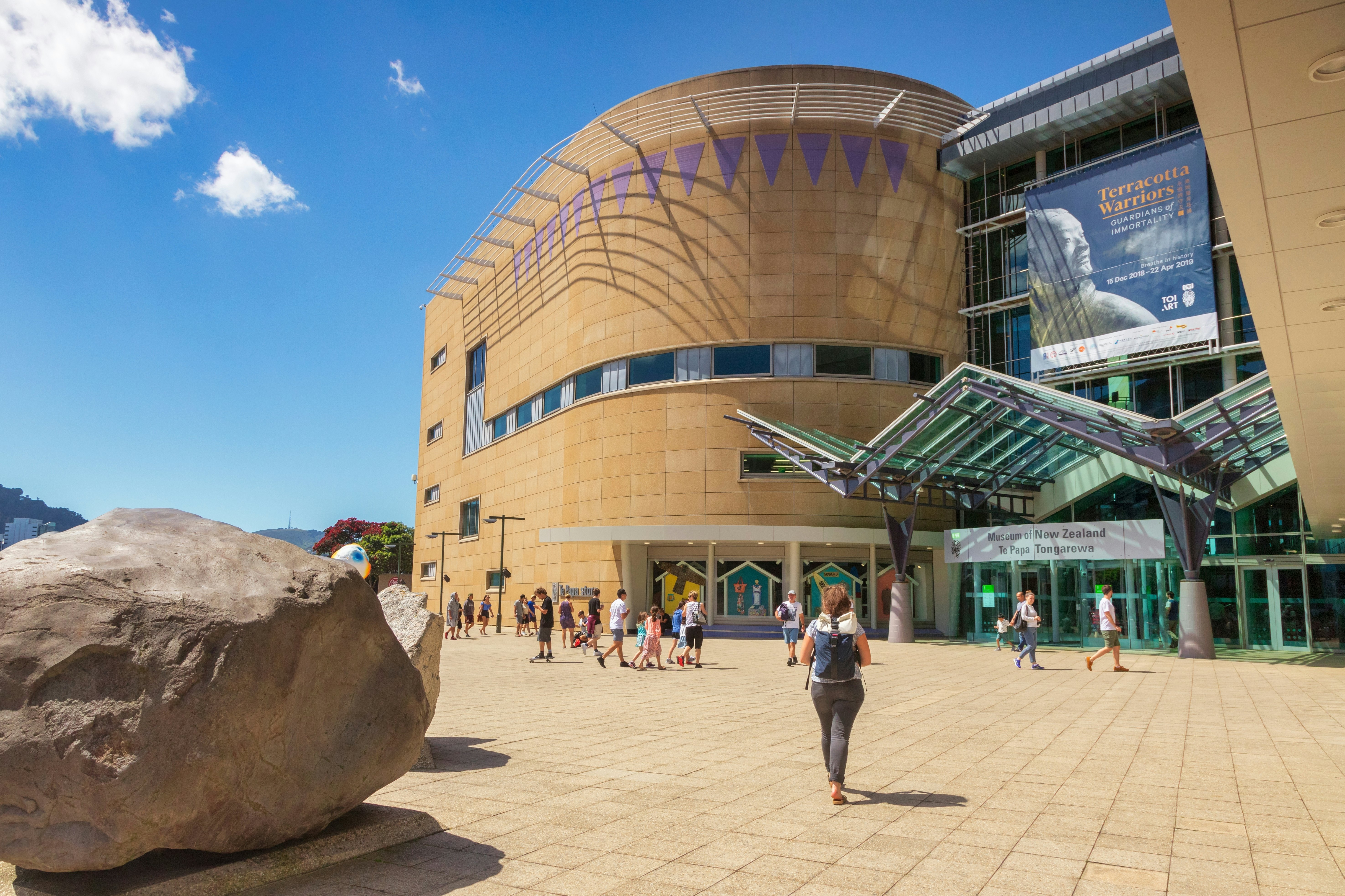 Tourists and visitors approach the entrance to a large museum building on a sunny day.