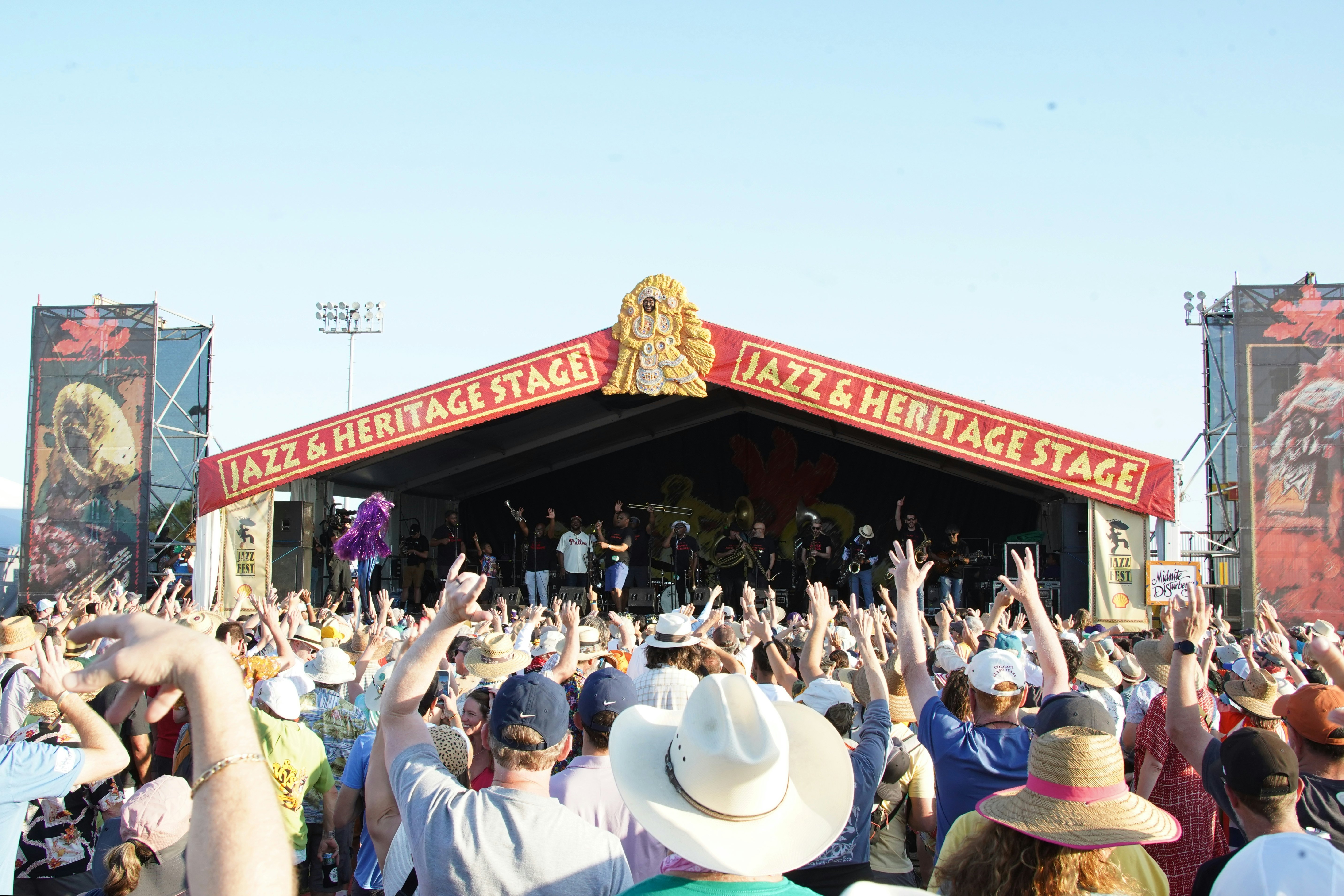 Crowds of people with their hands in the air watch musicians perform on stage at a festival.