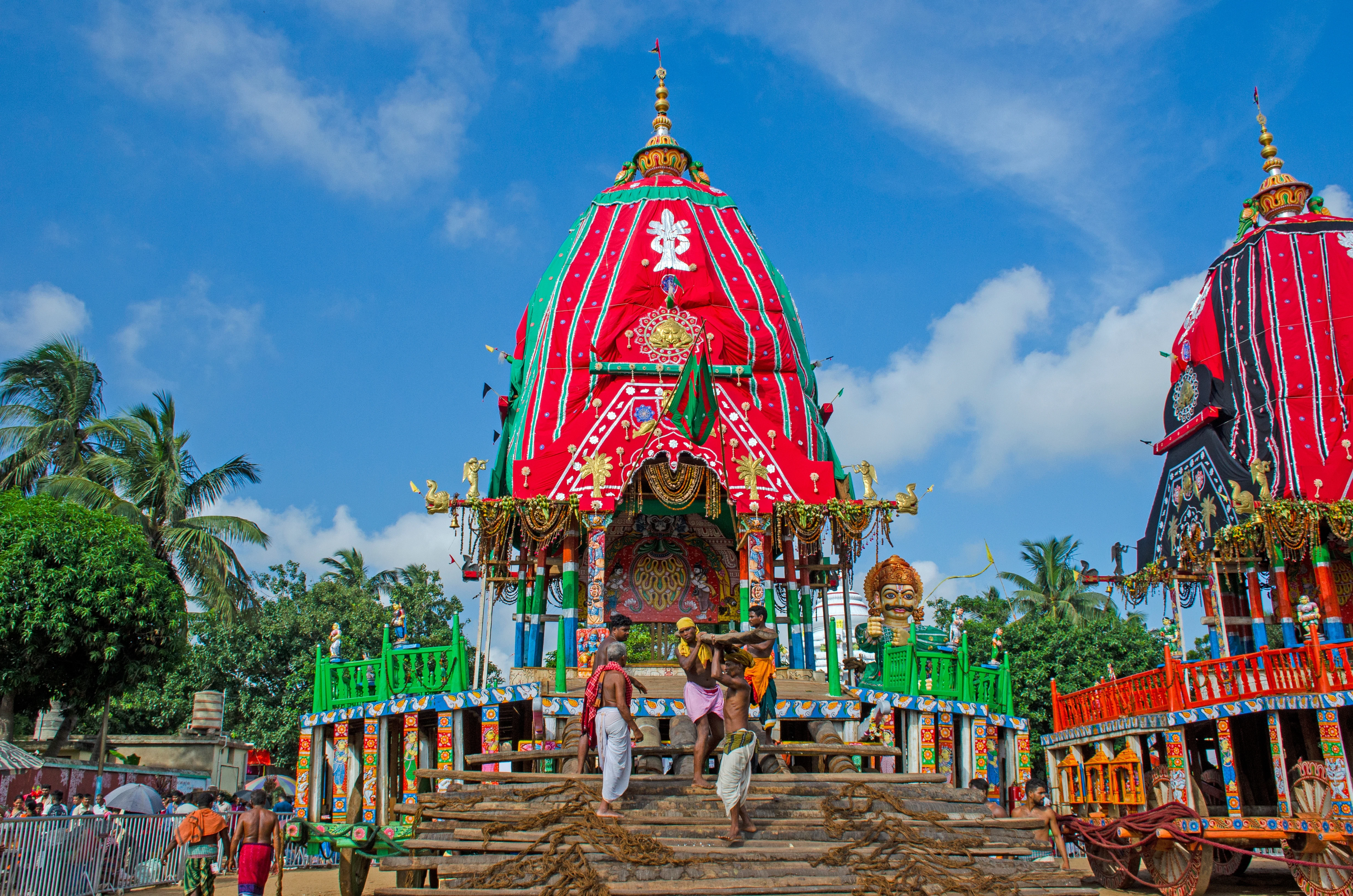 People stand on steps in front of an elaborately decorated temple tower.
