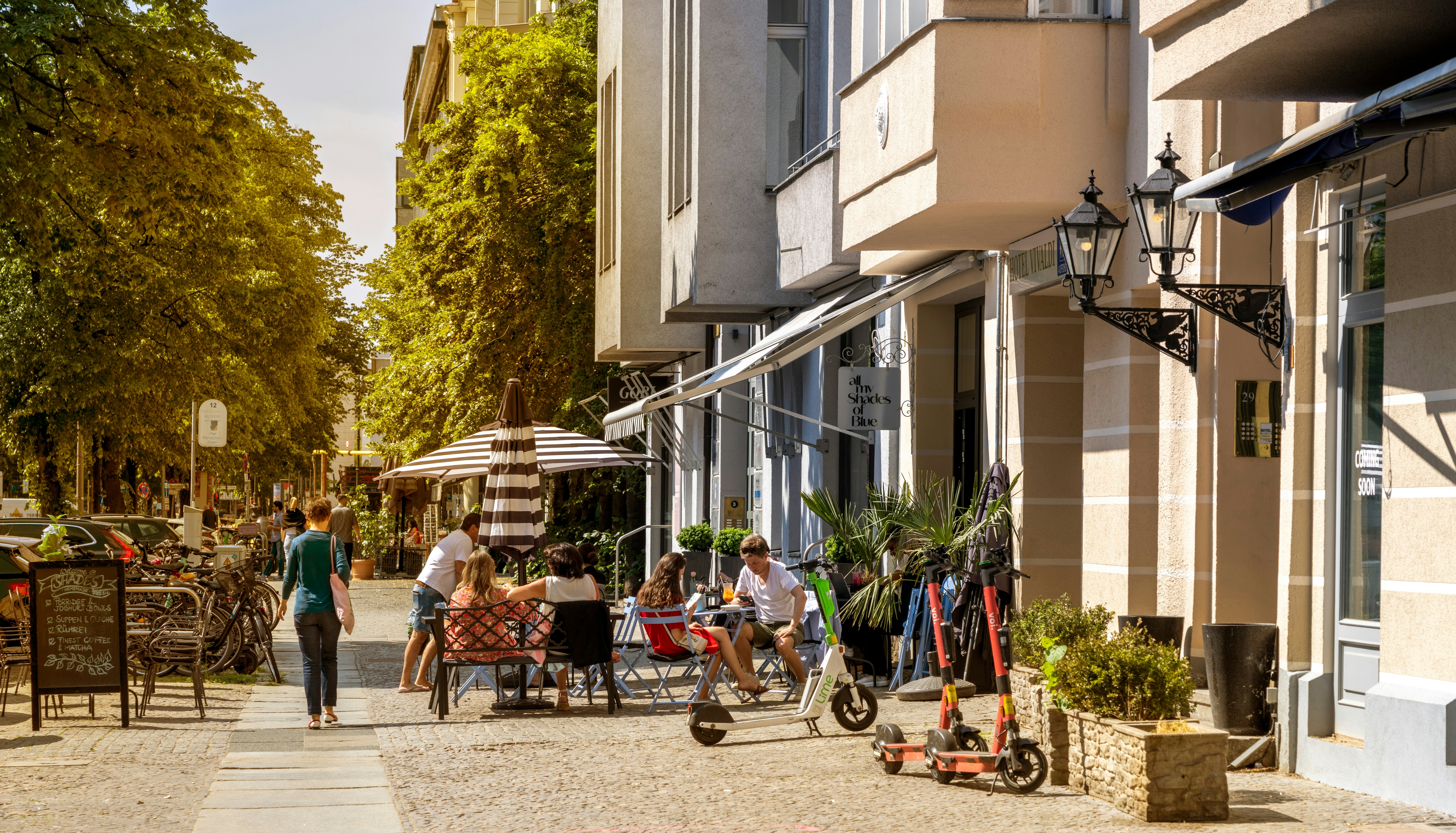 People sit at an outdoor table on a sidewalk in a city on a summer day.