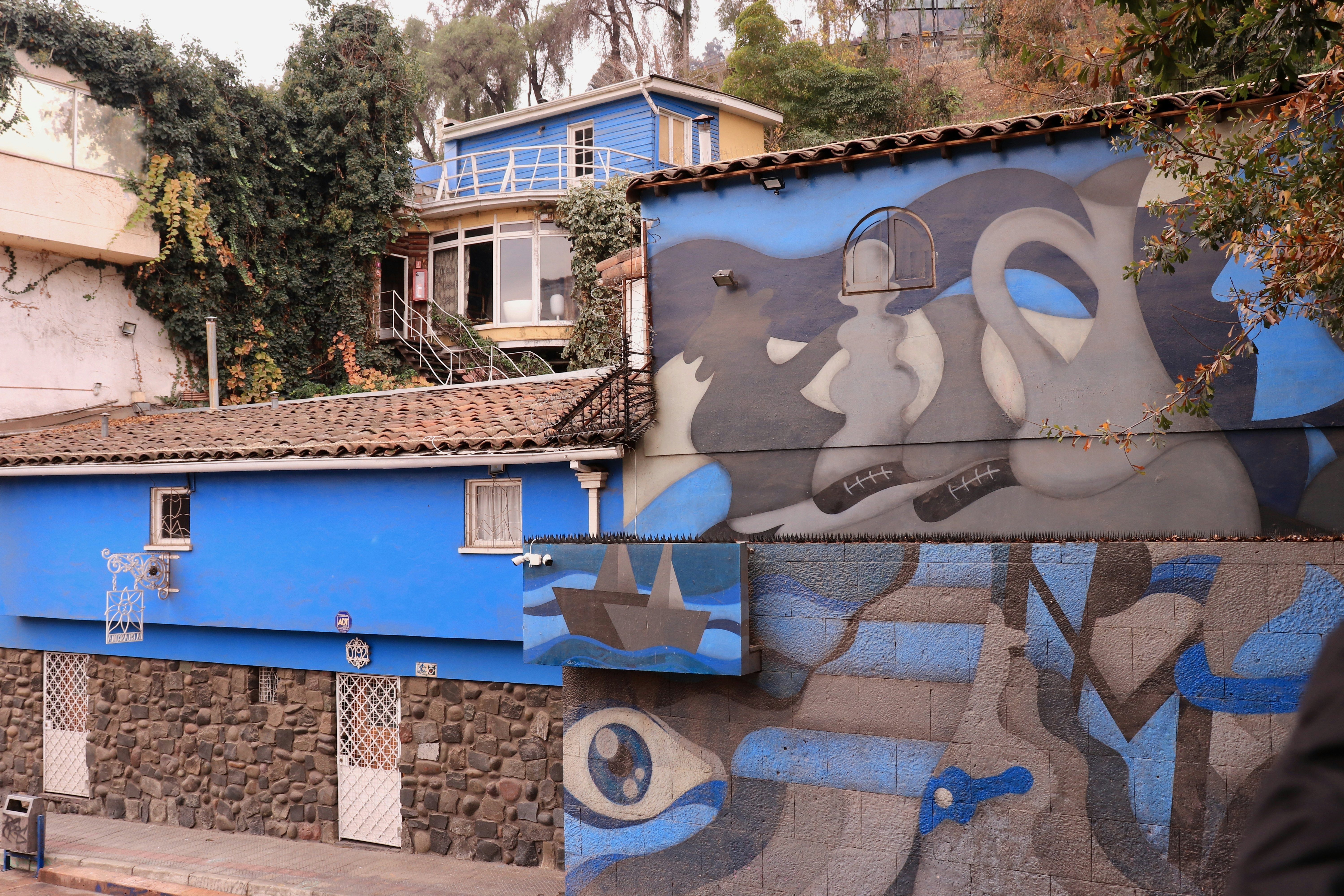 The exterior of a multilevel villa in a city, with one wall painted with a gray-and-blue mural.