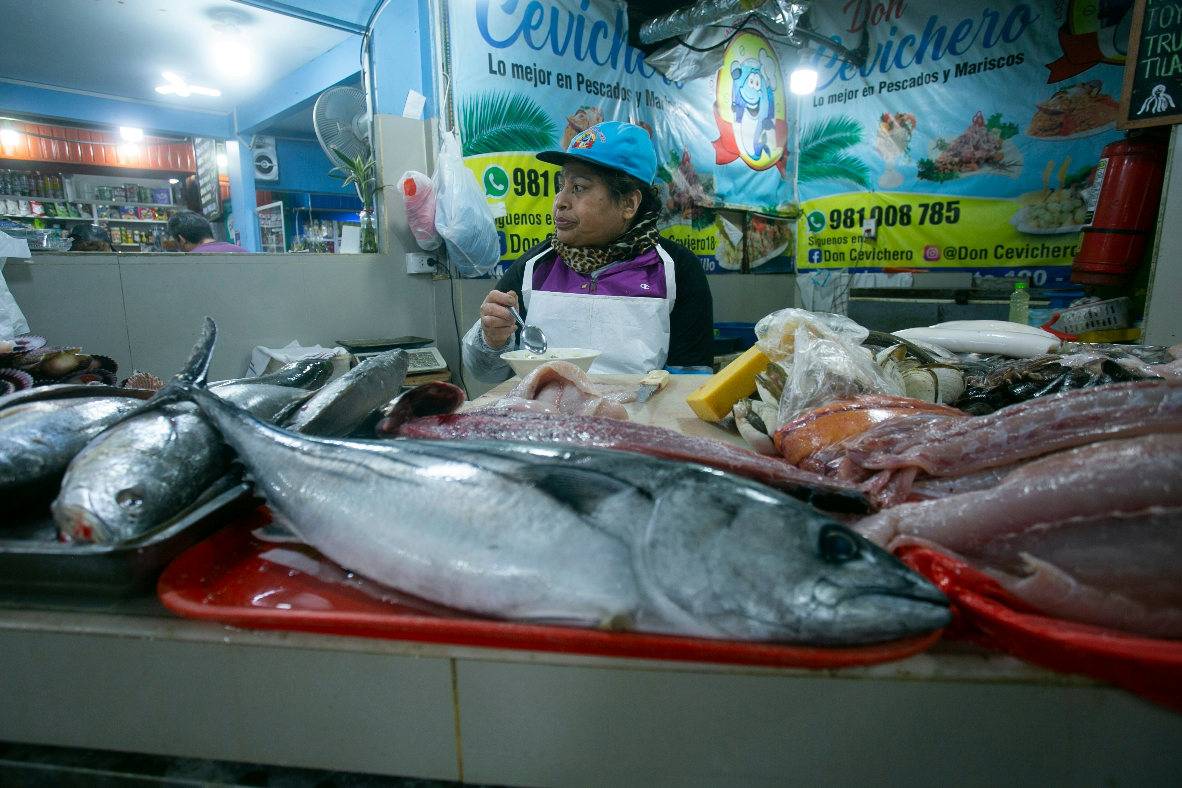 A vendor at a stall in a covered market sells huge fresh fish.