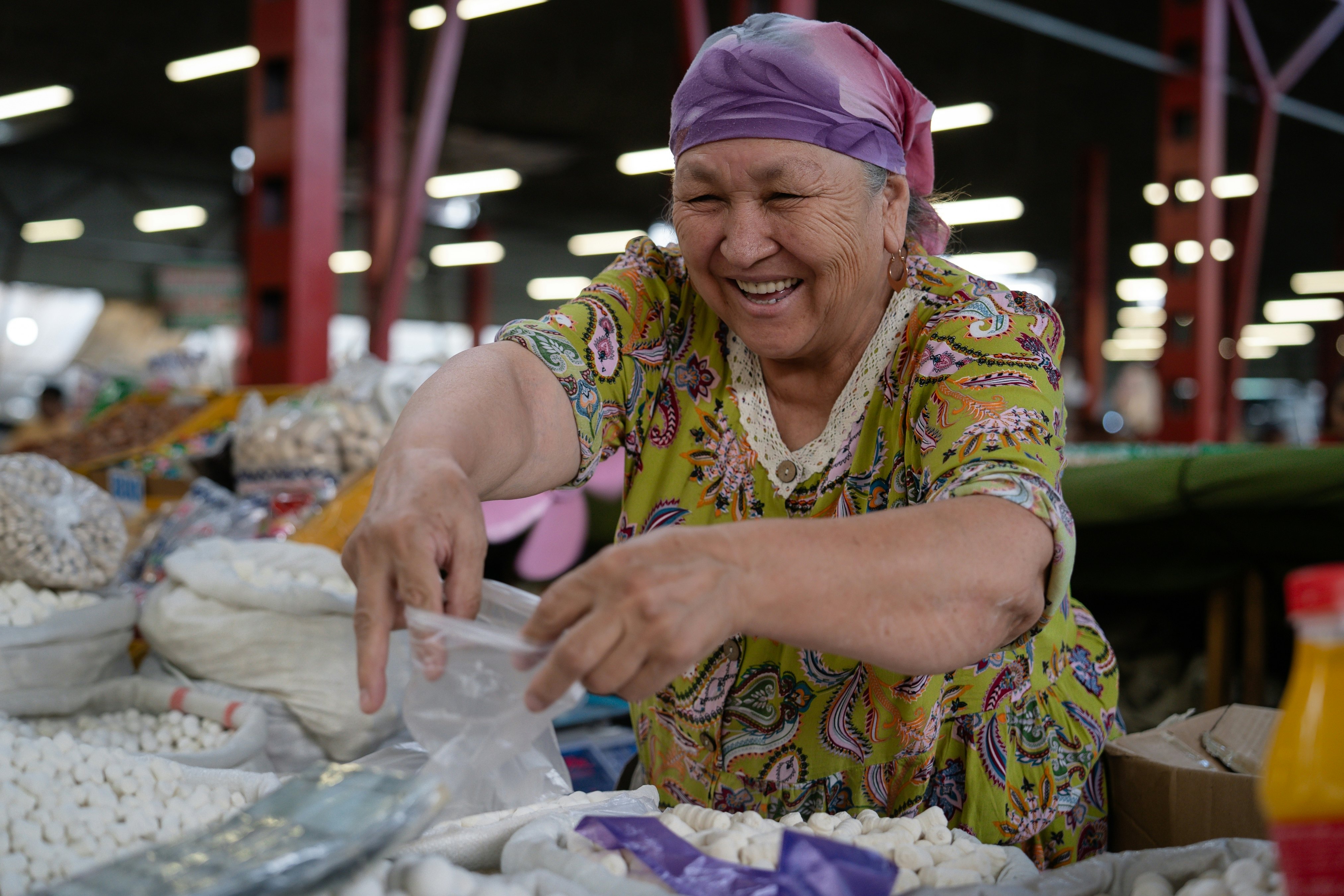 A smiling woman sells grains at a covered market.