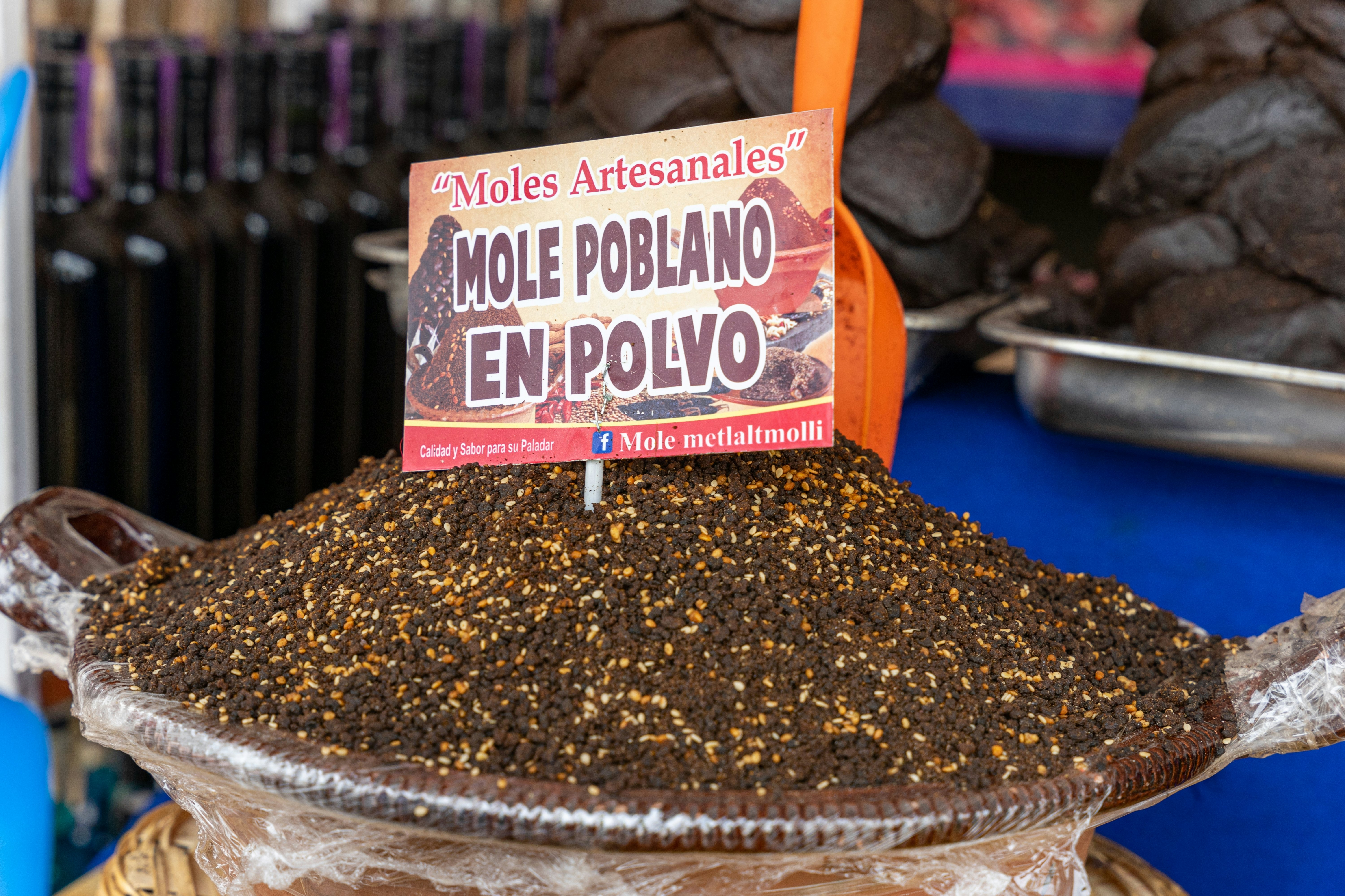 A bowl of powdered spices with a sign reading "Mole Poblano En Polvo" at a street vendor.