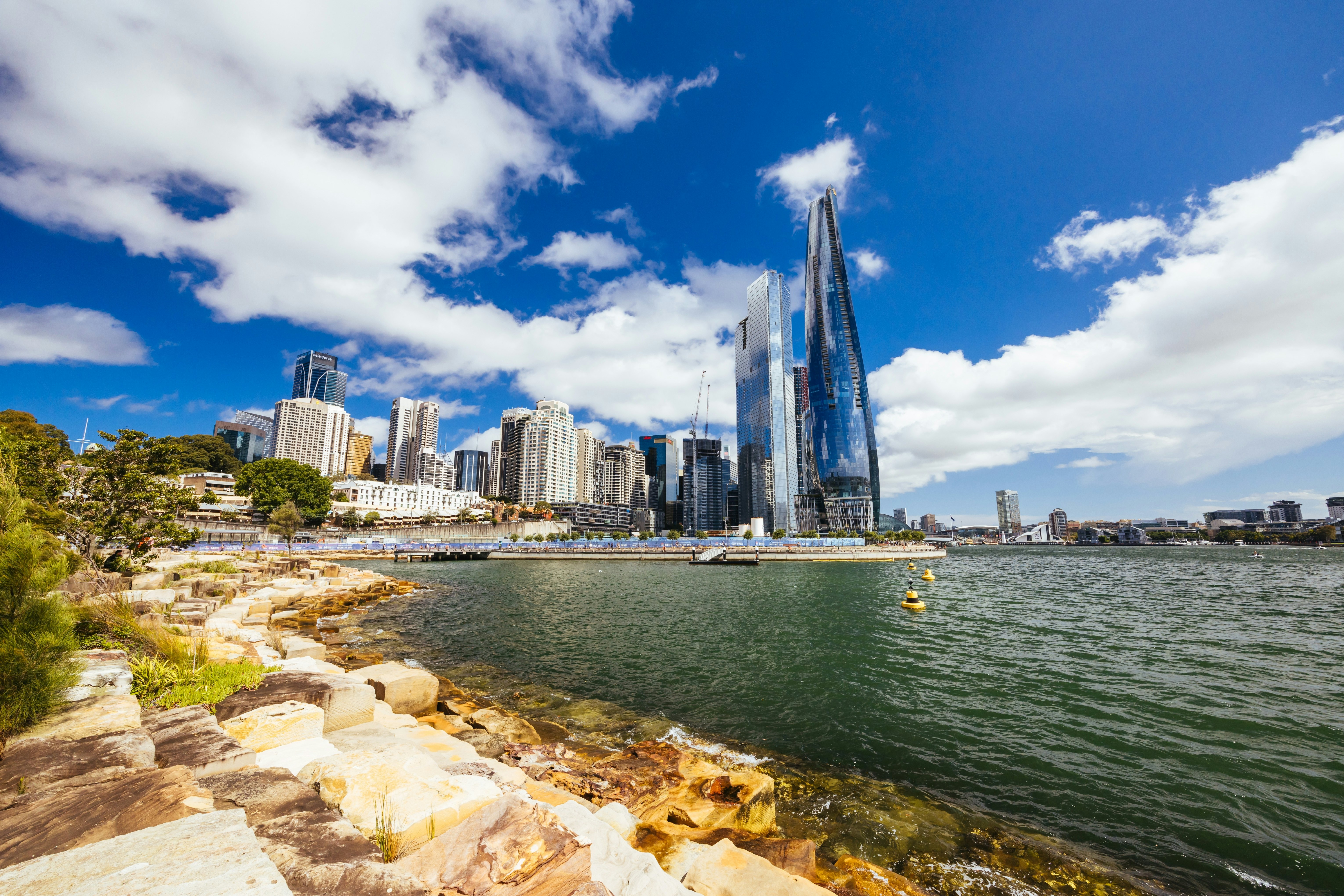 A rocky beach in a city, with skyscrapers seen across the water.