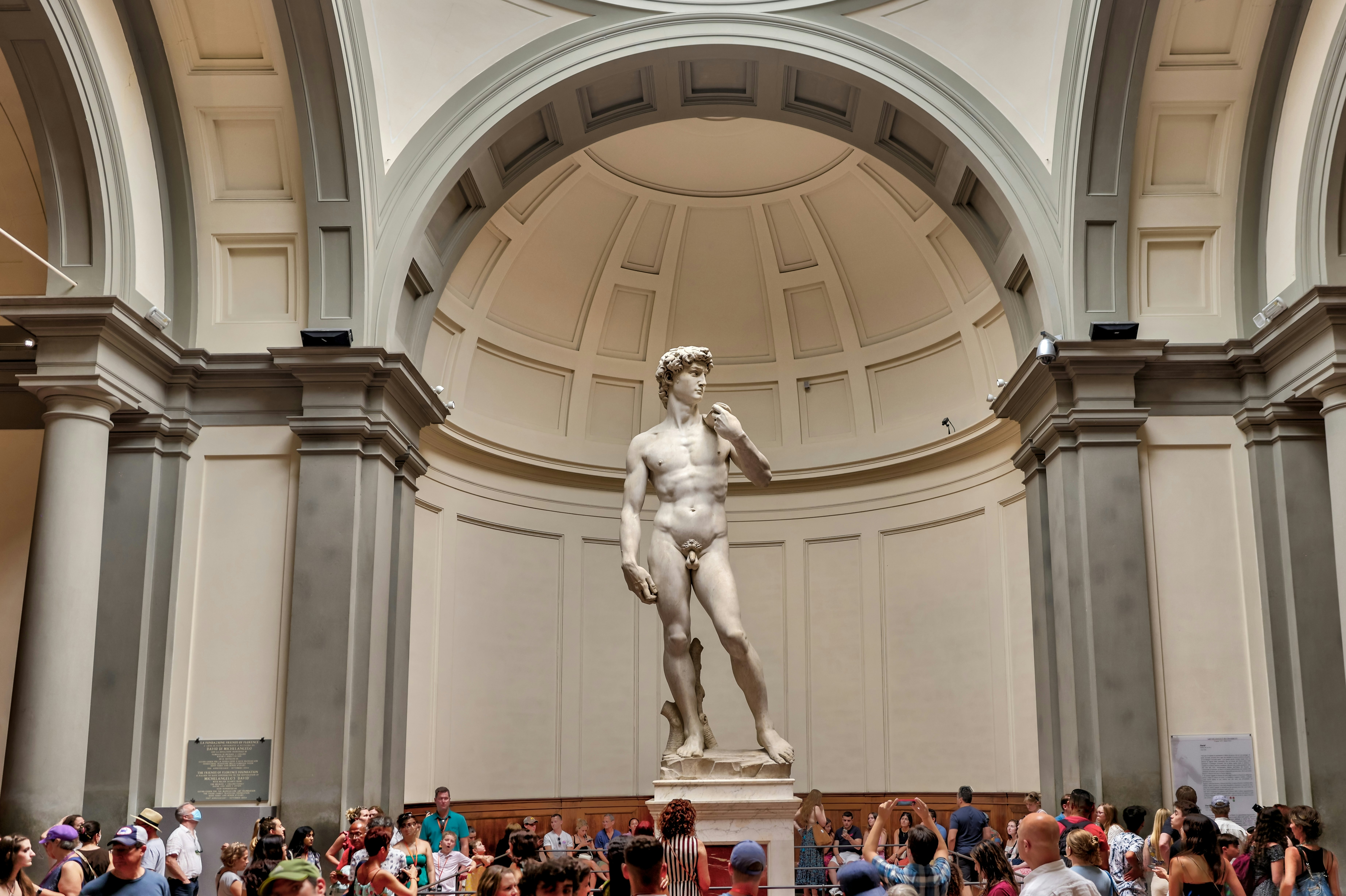 People in a gallery take photos of the marble statue of David