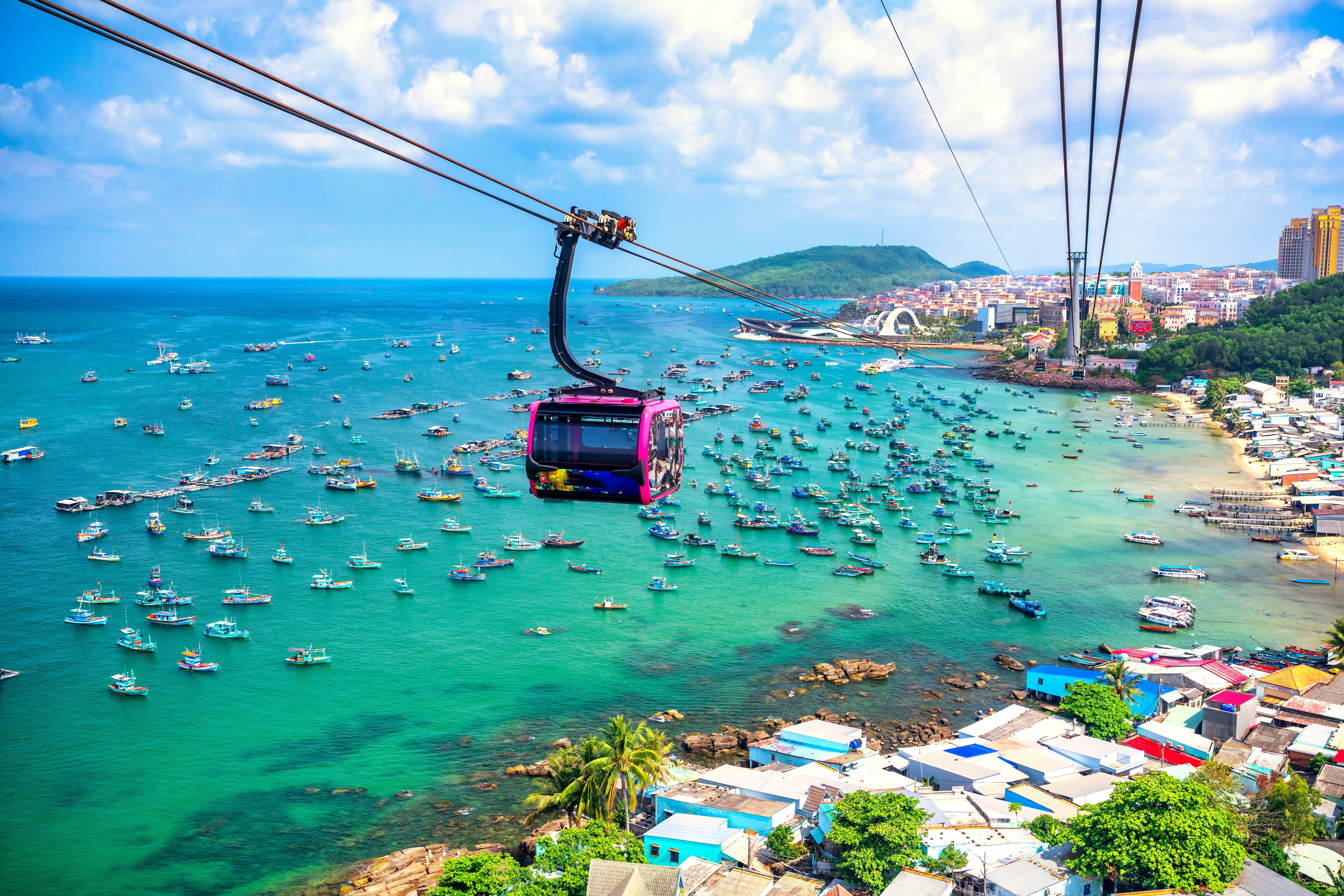 A cable car travels over a bay that's filled with small boats.