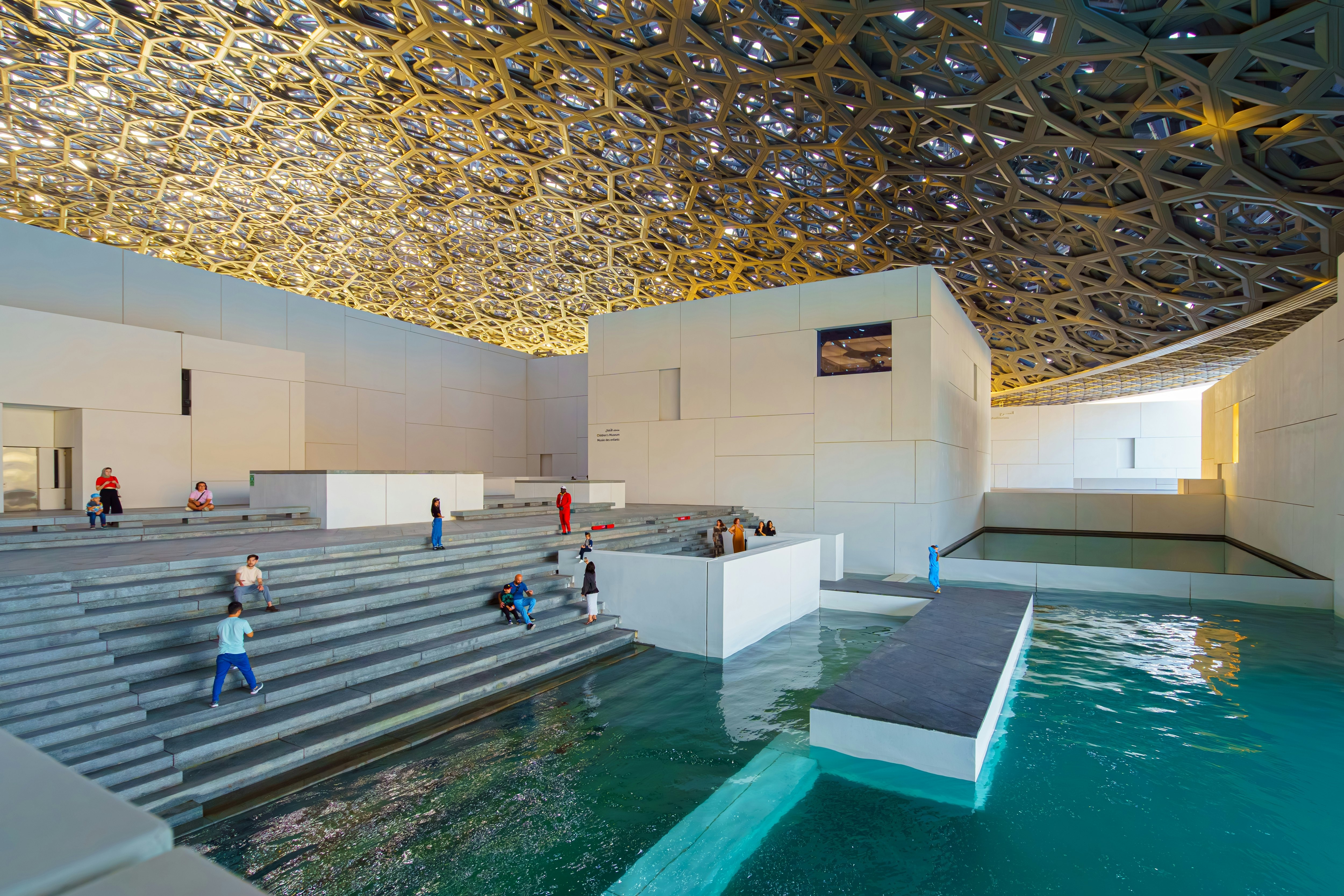 A museum with steps down to a vast indoor water feature and a detailed mesh ceiling.