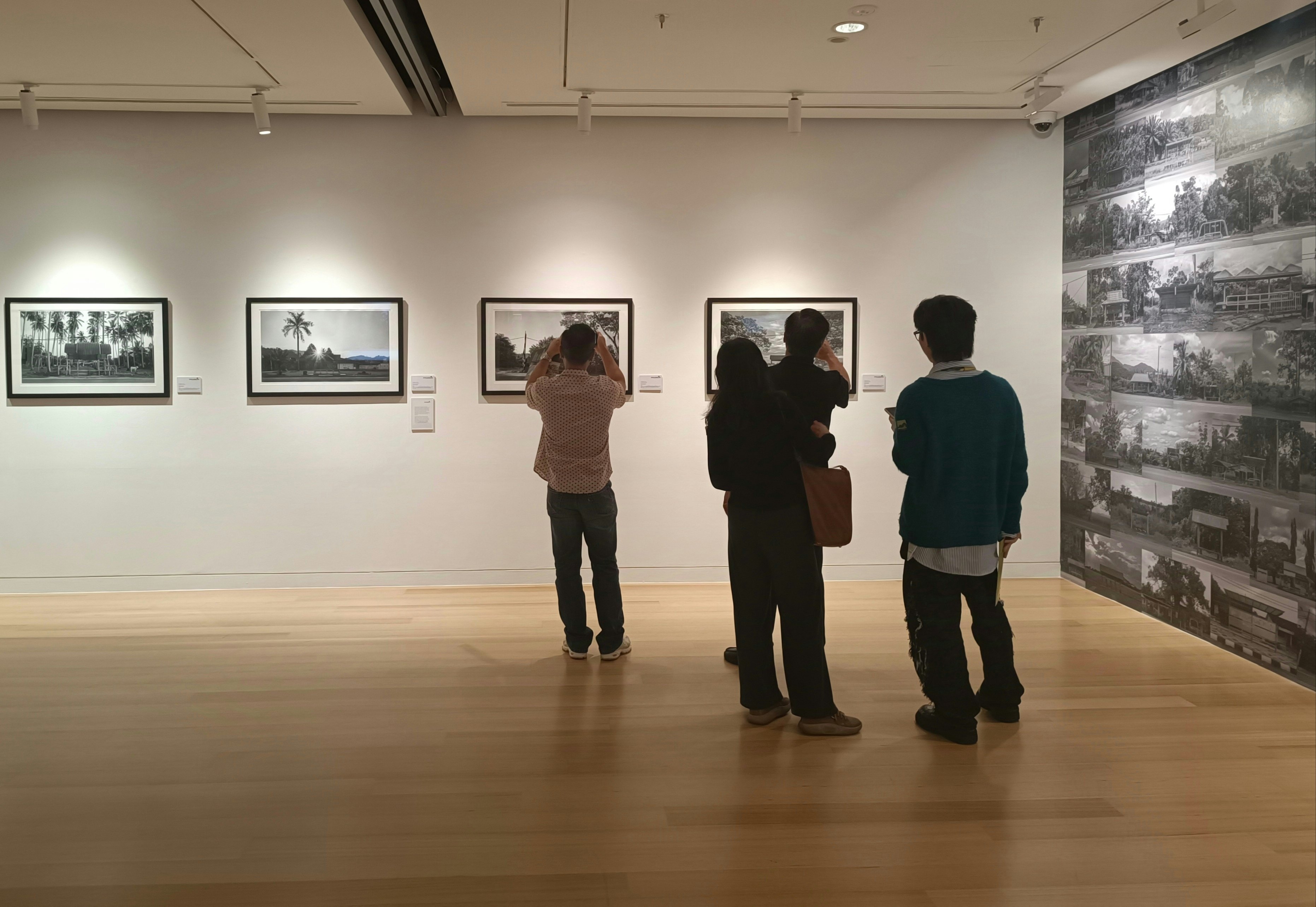 People in a gallery admire photographs mounted on a white wall.