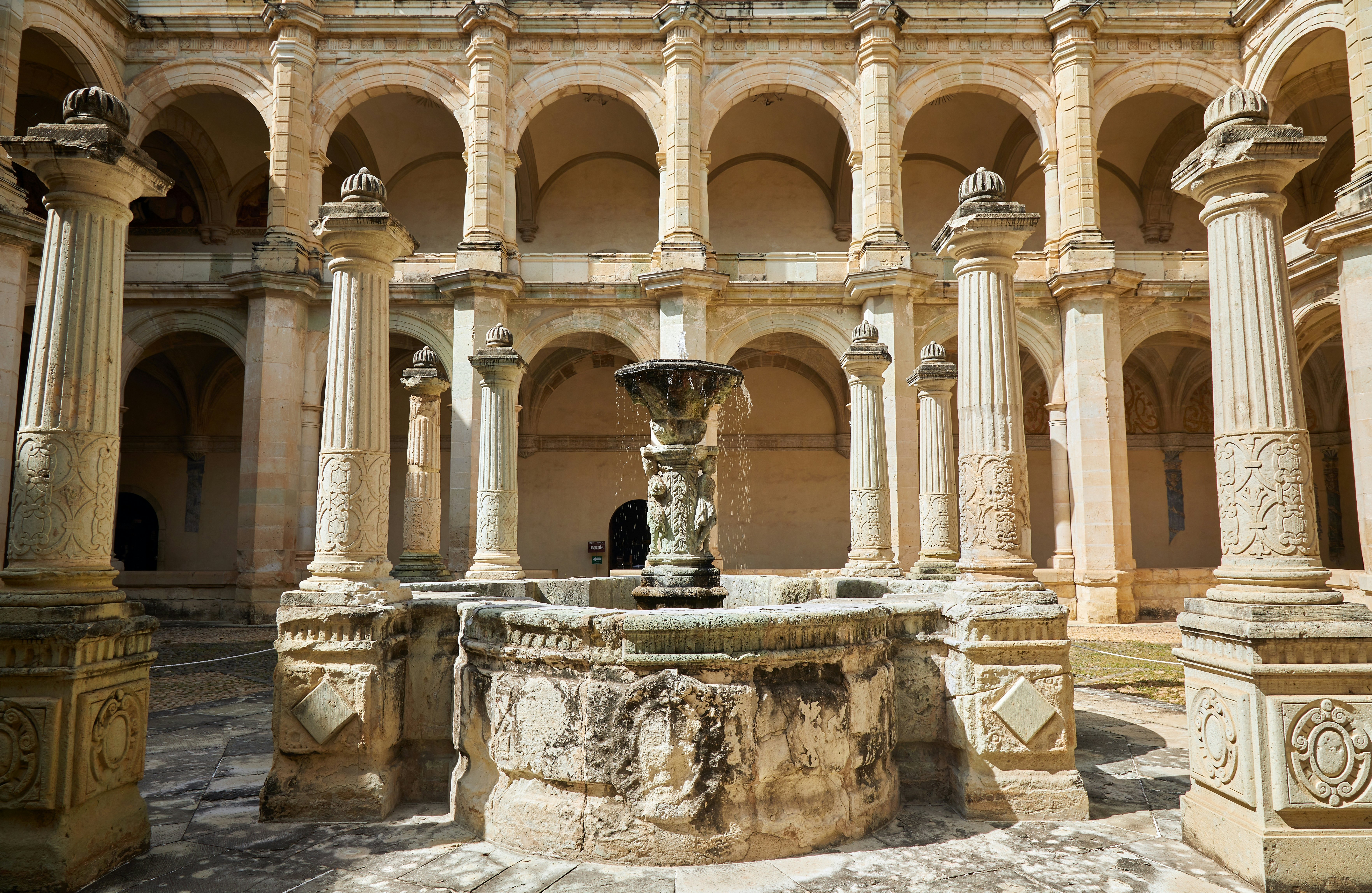 Courtyard with a fountain surrounded by baroque sculpted pillars on a sunny day.