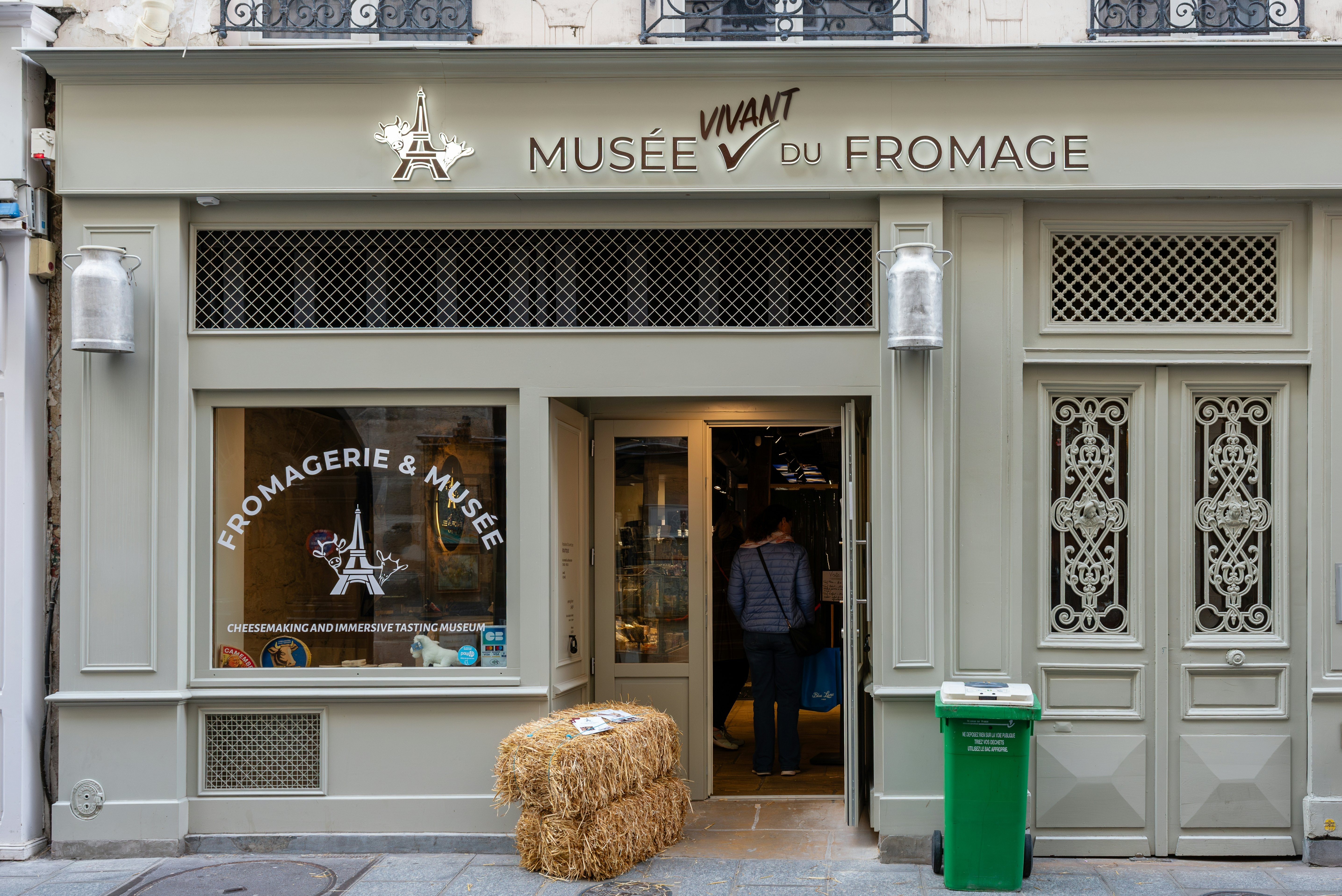 A shop front-style entrance to a museum with cow graphics on the window and two bales of hay outside.