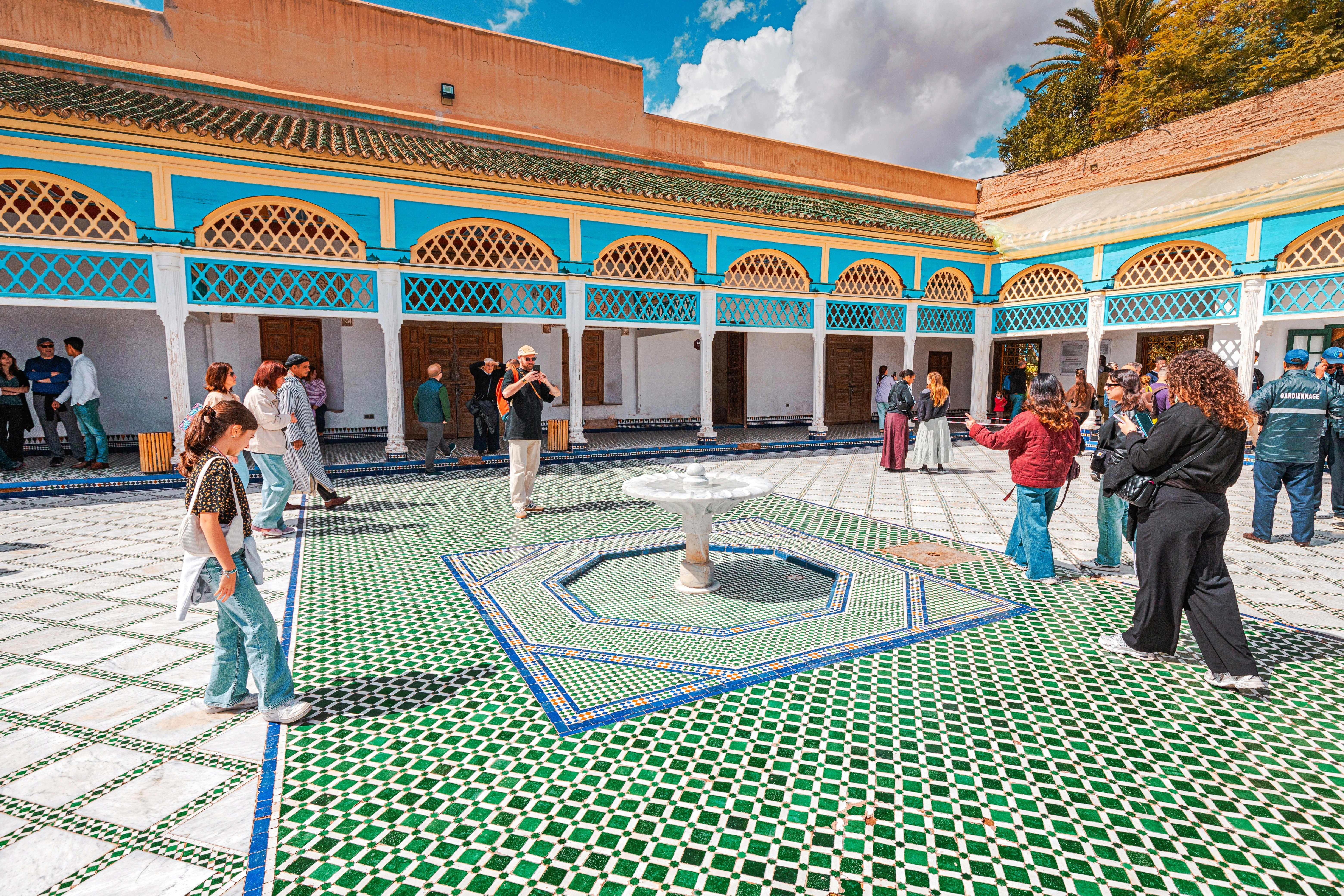 Marrakech, Morocco: Tourists walking in the courtyard with fountain and zellige tilework of the Bahia Palace.