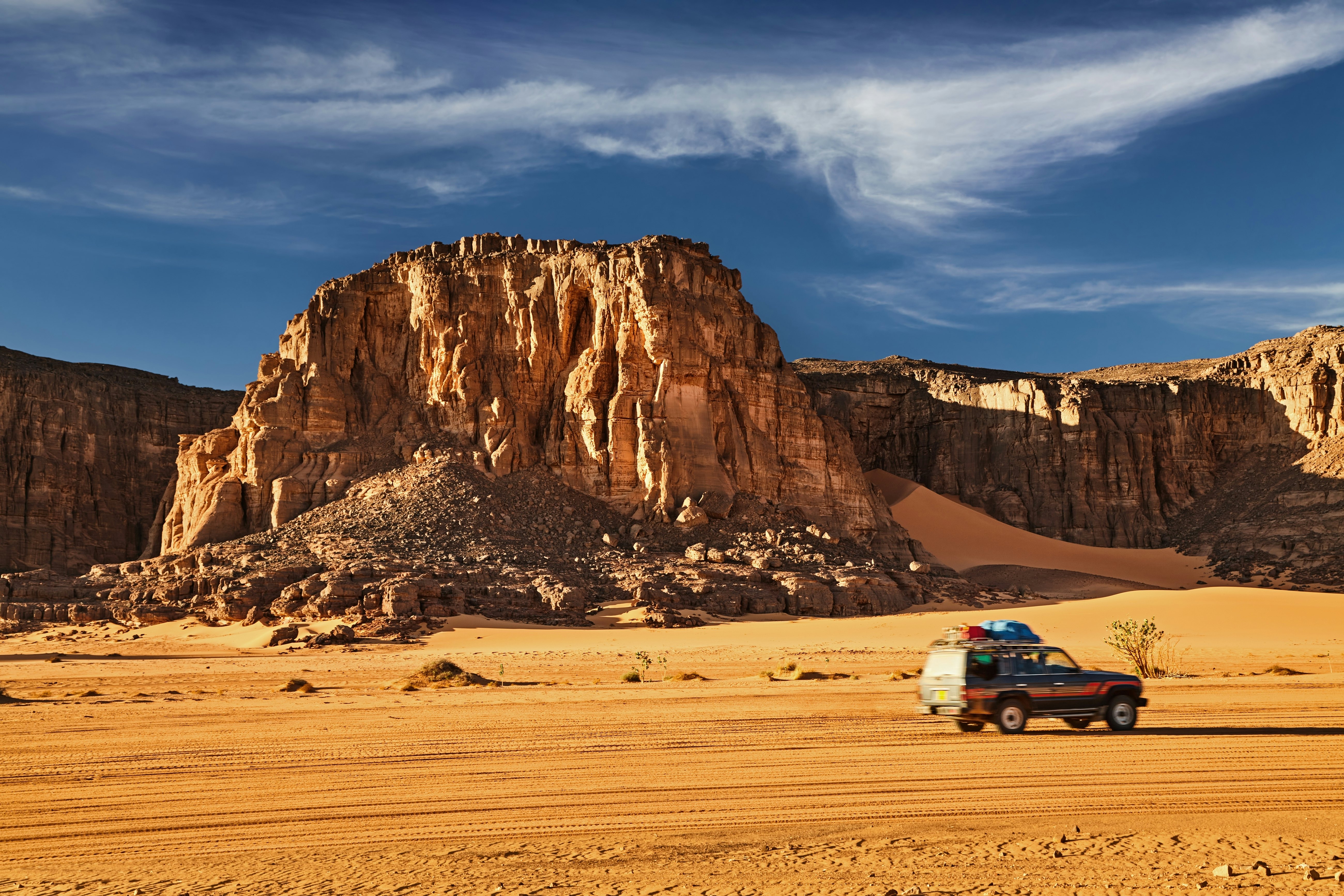 Road in Sahara Desert, a car drives among the rocks and sand dunes, Tadrart, Algeria.