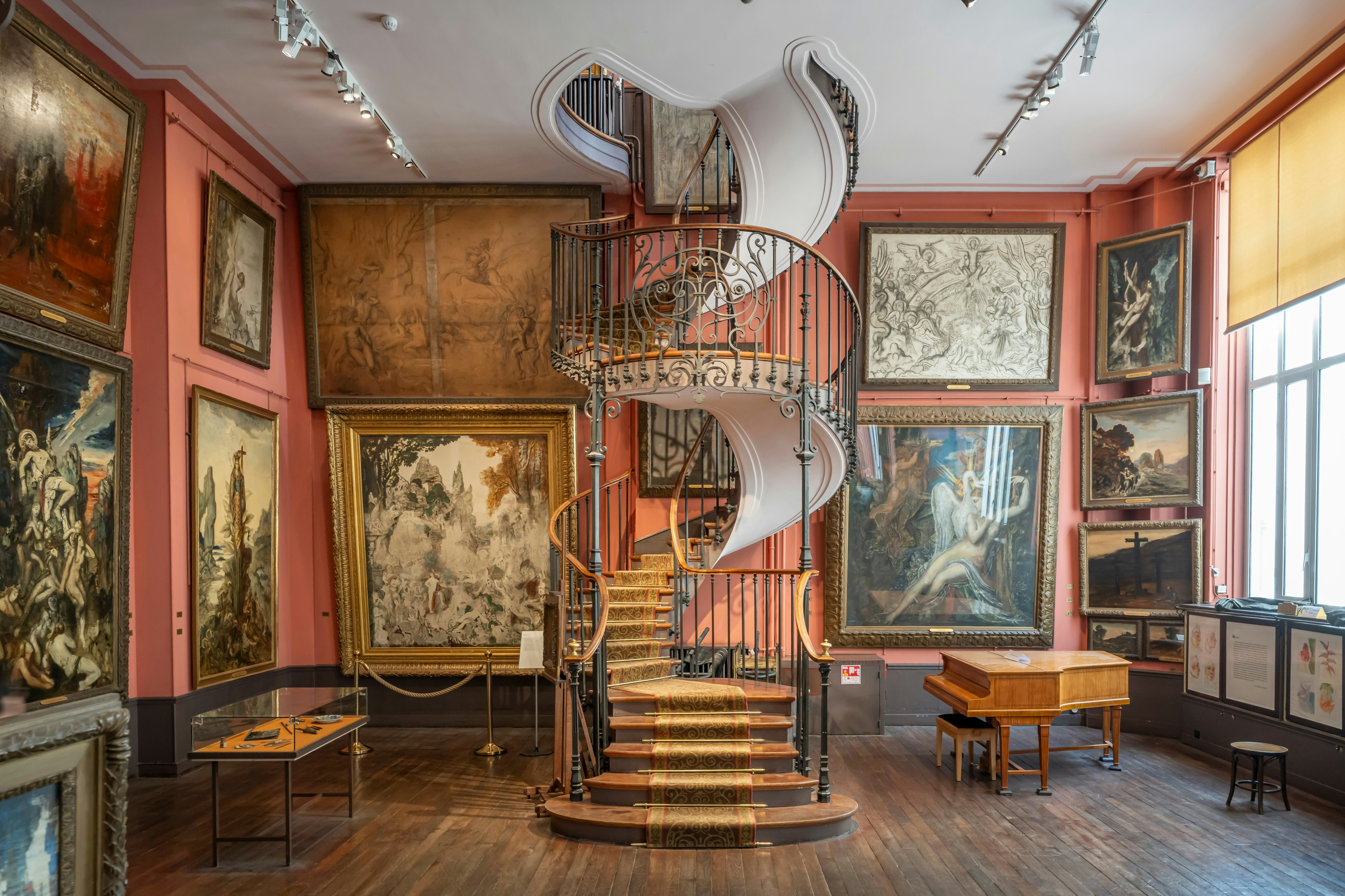A stunning spiral staircase with wrought-iron banisters in an artists studio with large oil paintings on the walls.