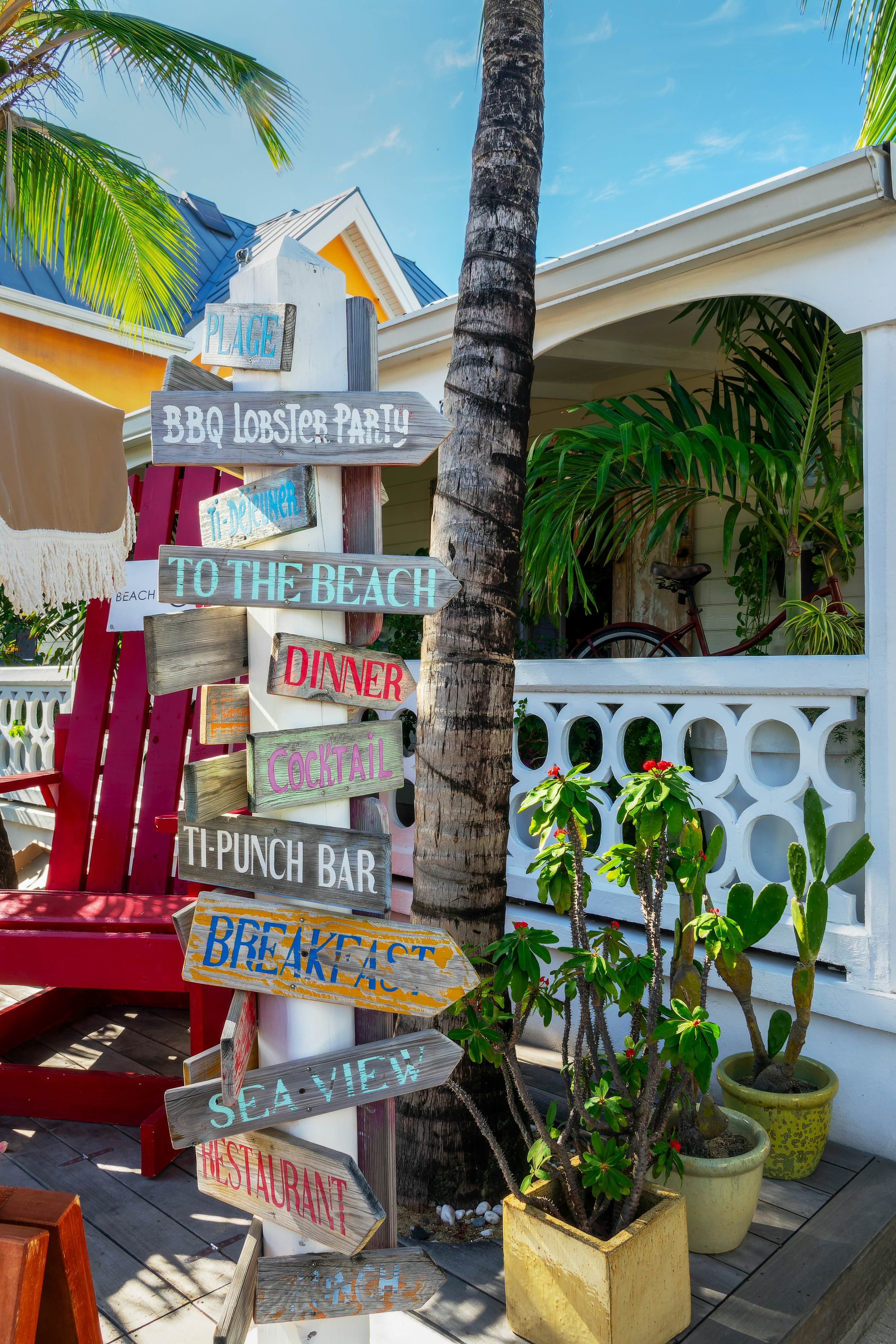 Wooden signs with hand-painted words, like "To the beach" or "Punch bar." The signs all hang on one post and point in various directions.