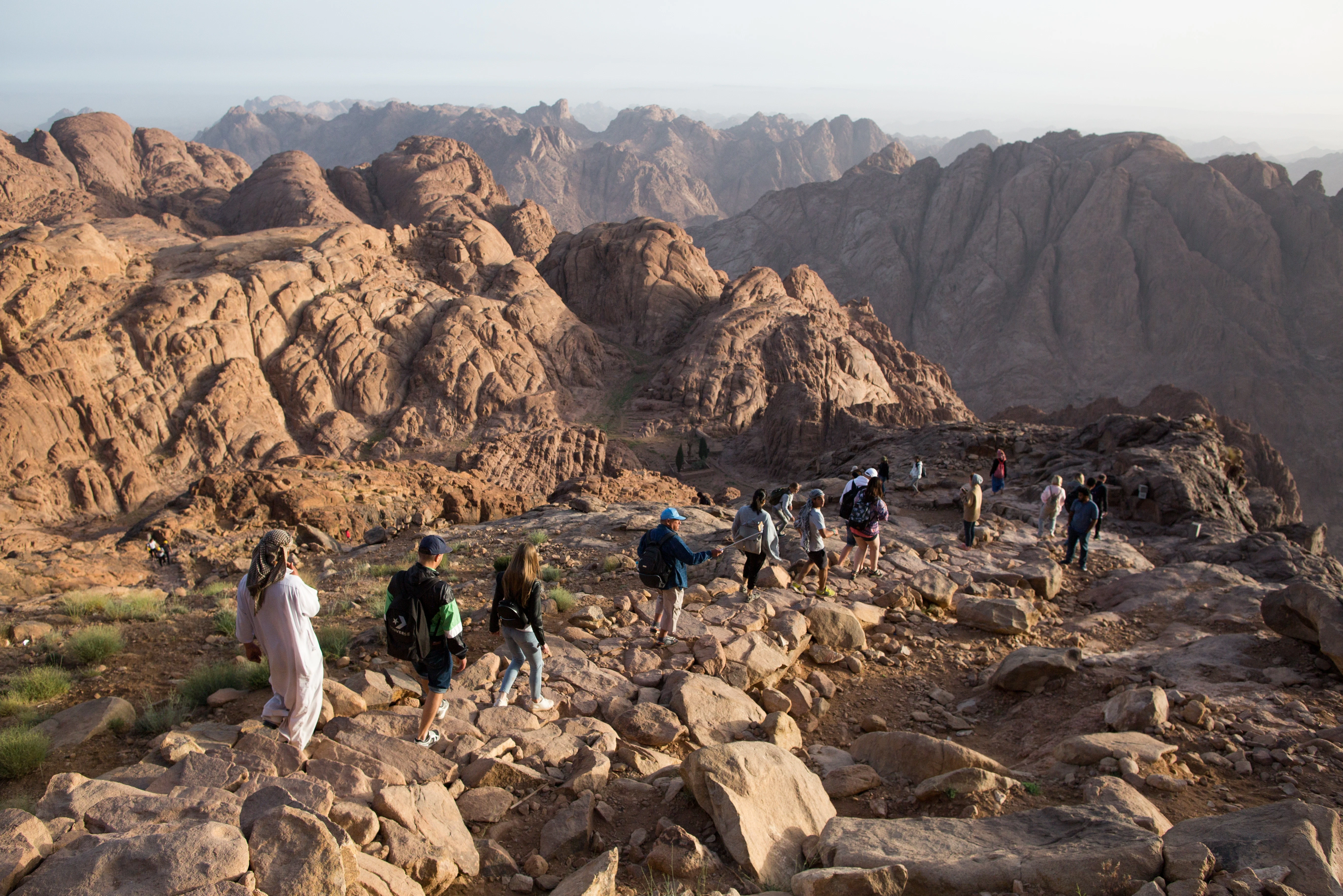 A group of tourists walks on a rugged mountain path on Mt Sinai in Egypt at sunrise.