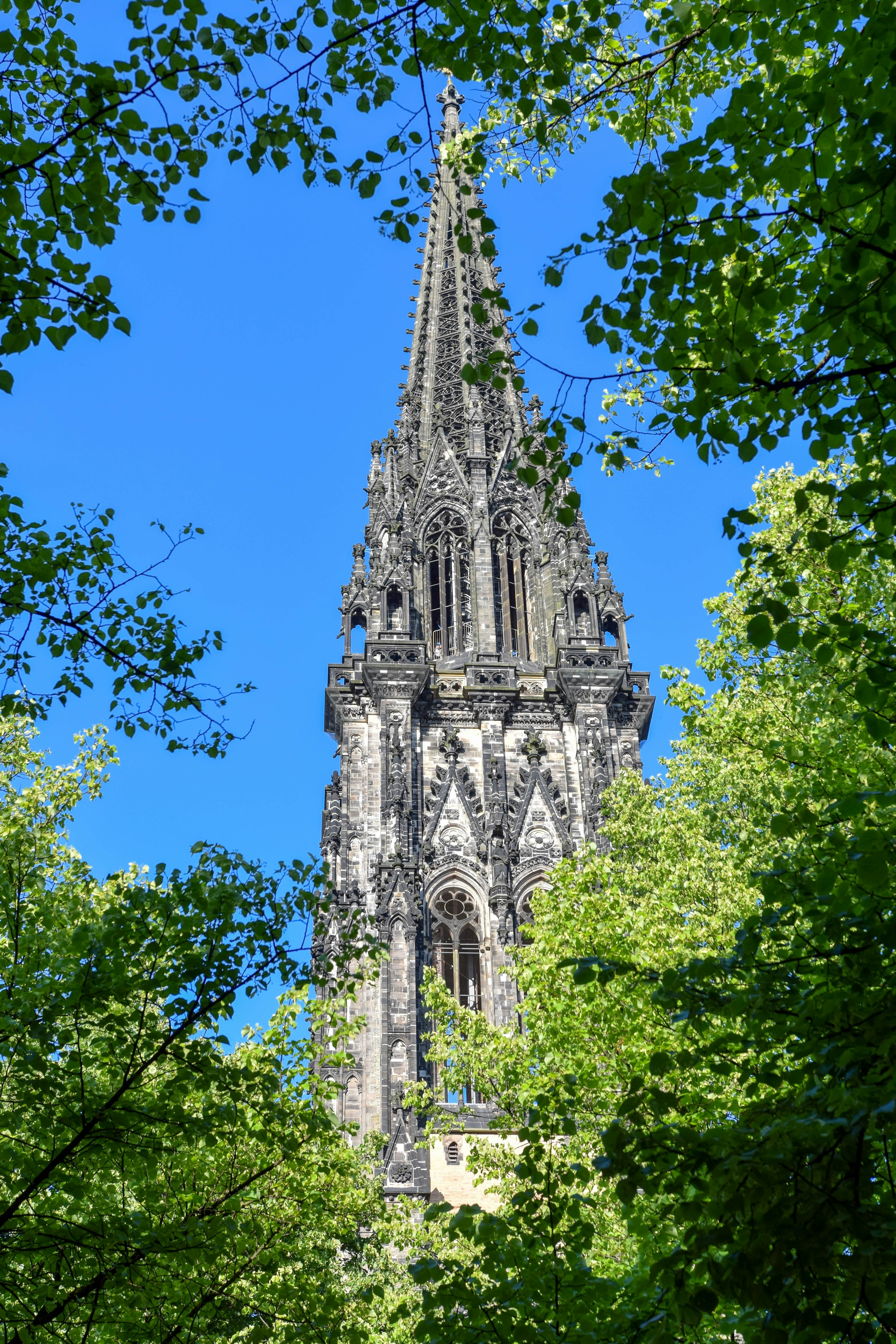 View of an ornate church tower through treetops on a sunny day.