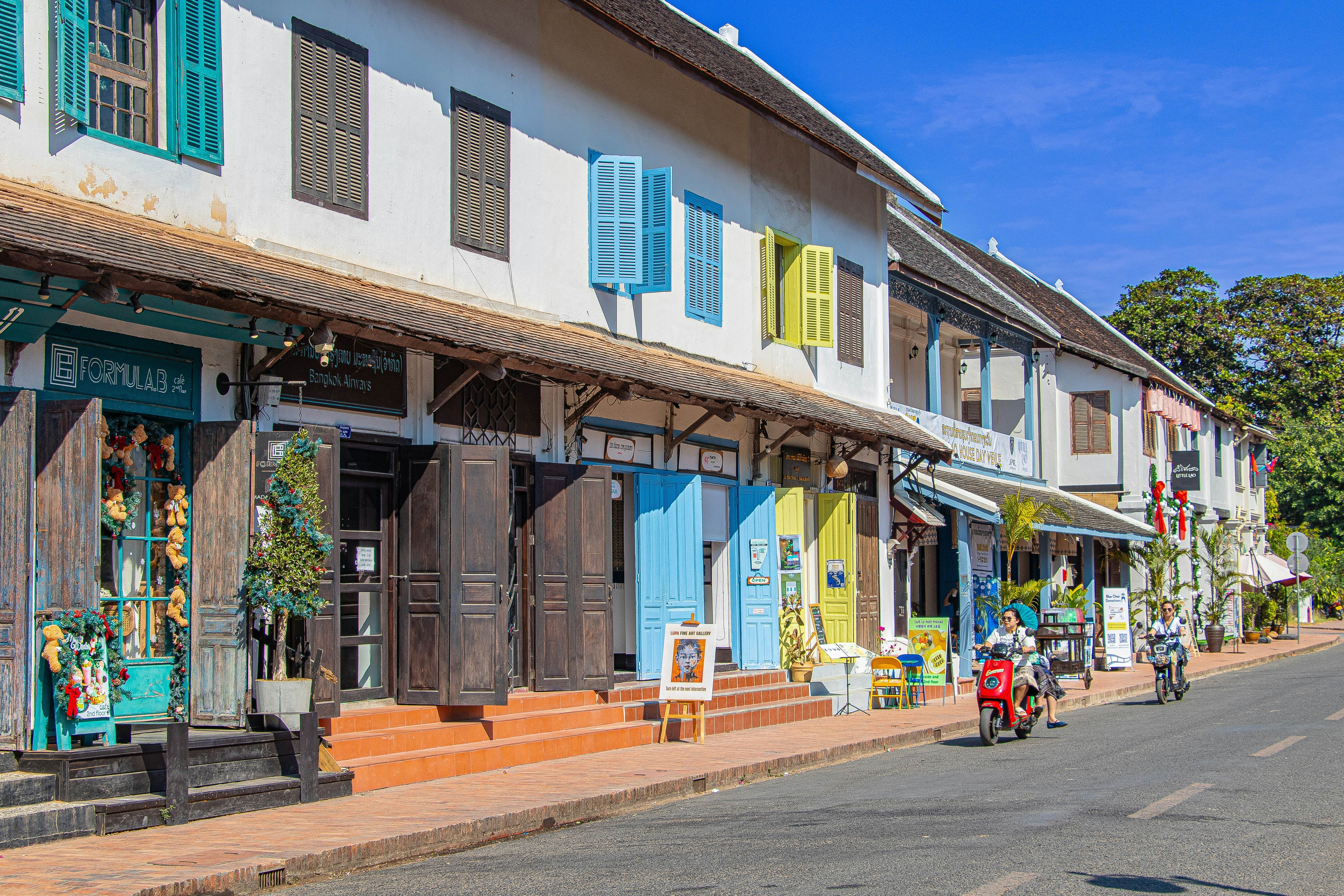 Luang Prabang, Laos - November 22, 2025: Colorful colonial-style street in Southeast Asia with people walking, scooters, and tuk-tuks on a sunny day., License Type: media, Download Time: 2025-11-25T19:03:00.000Z, User: Malecia.Elamin_Lonelyplanet, Editorial: true, purchase_order: 65050 - Digital Destinations and Articles, job: Online editorial, client: Guide to Luang Prabang, Laos, other: Malecia Walker