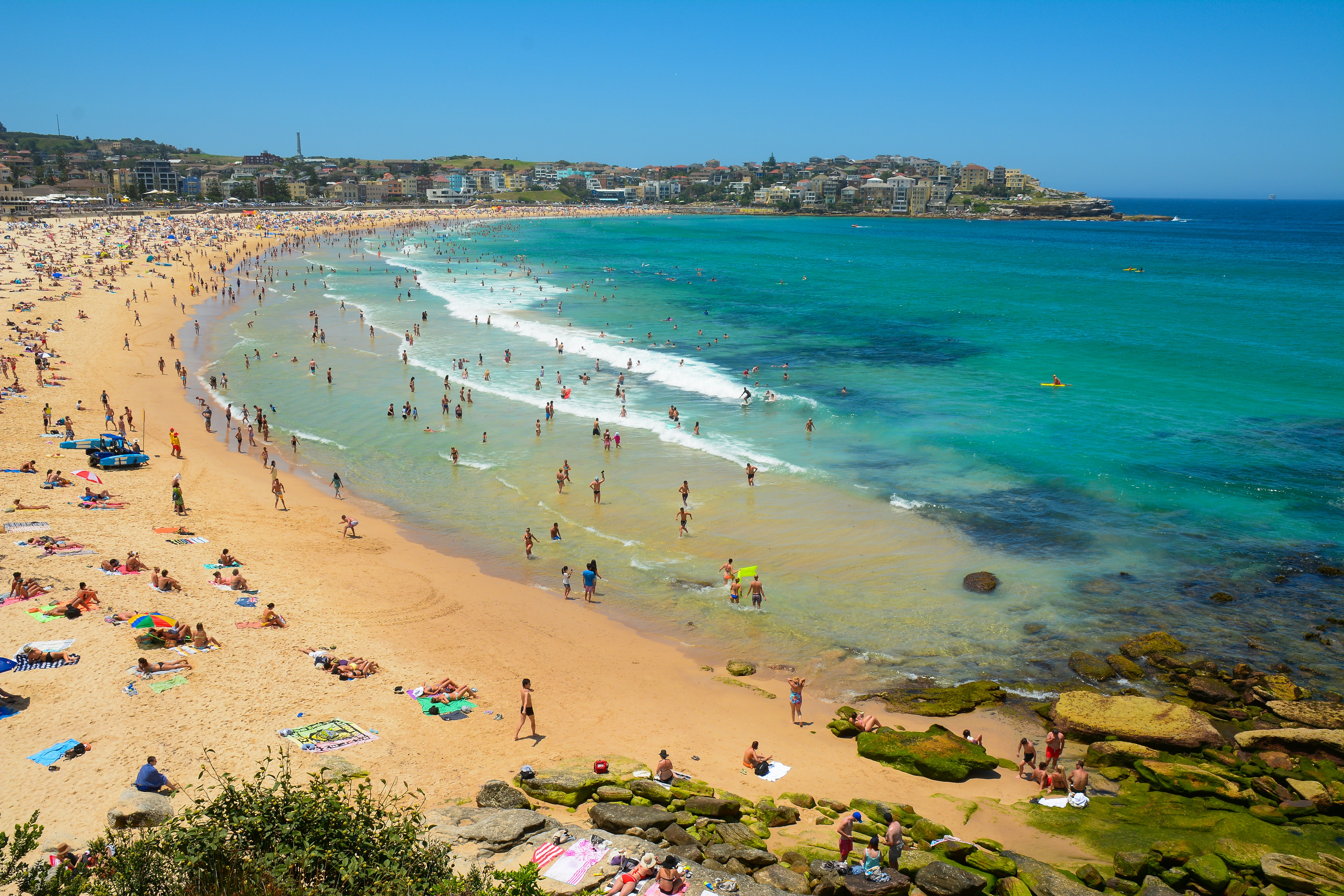 An aerial view of a crescent-shaped beach packed with people on the sand and in the water.