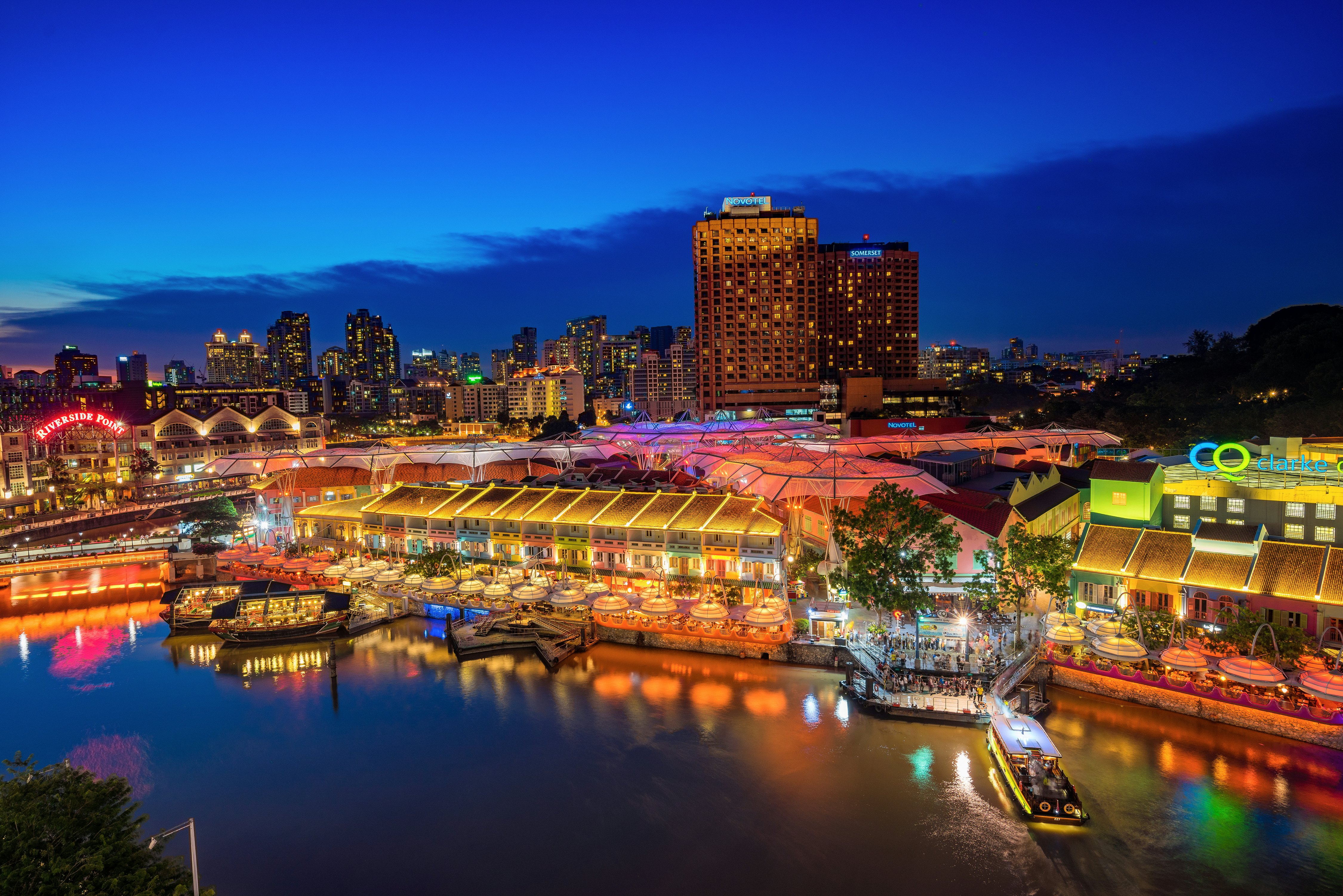 An evening scene of buildings colorfully lit by a river in a city.