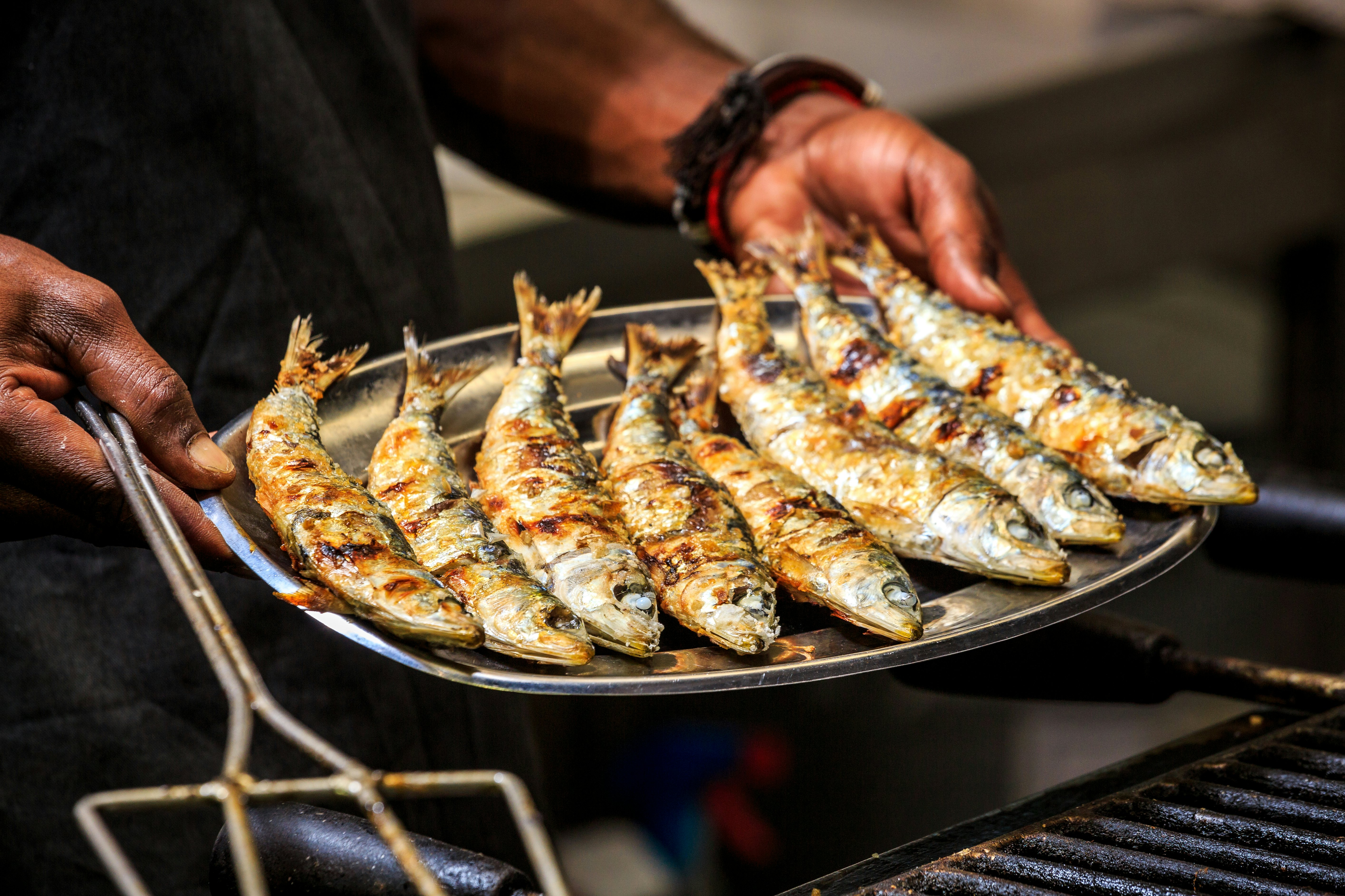 A chef holds a silver tray loaded with grilled fish.