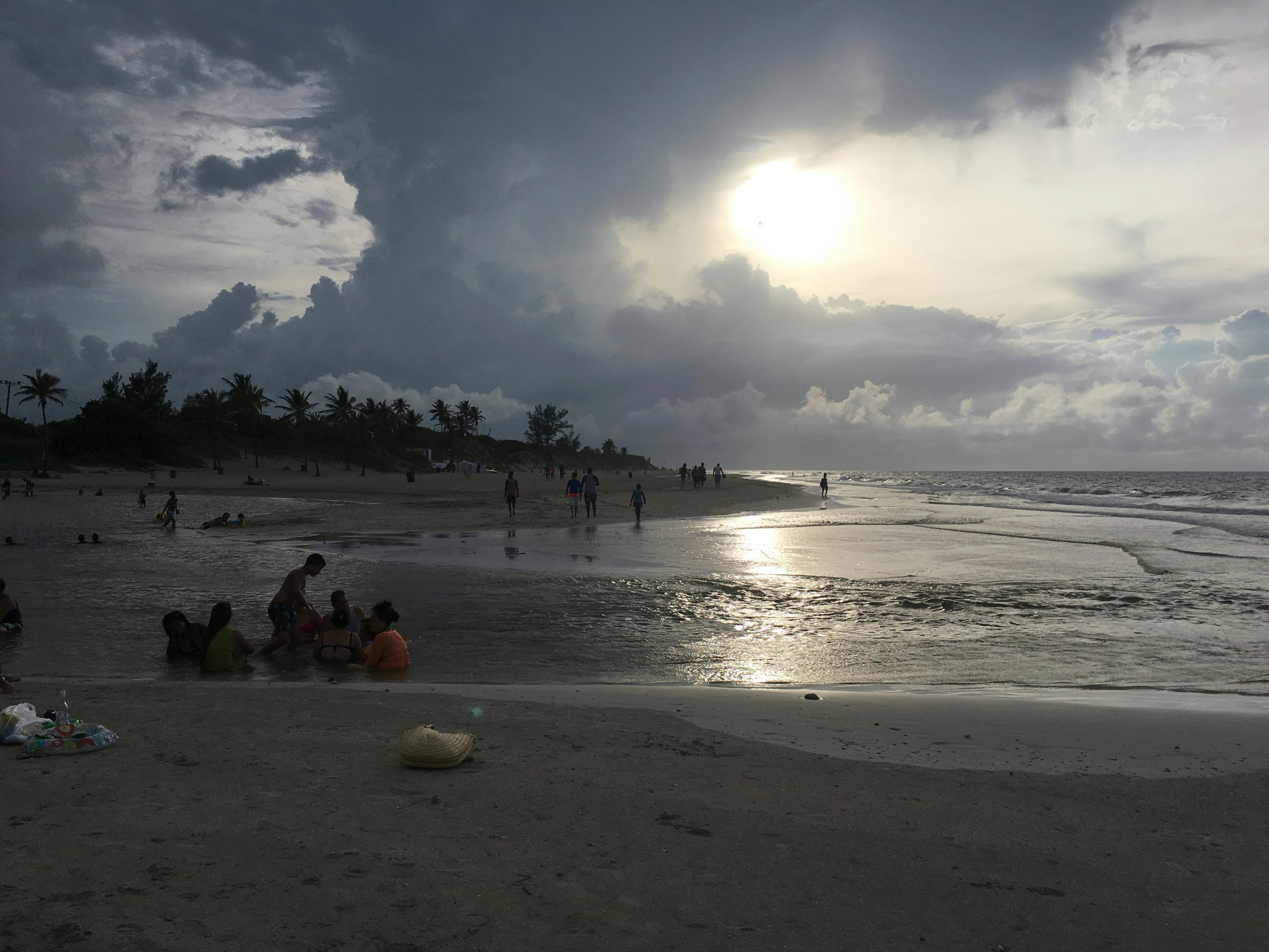 People walking and sitting by the shoreline of a beach on a cloudy day