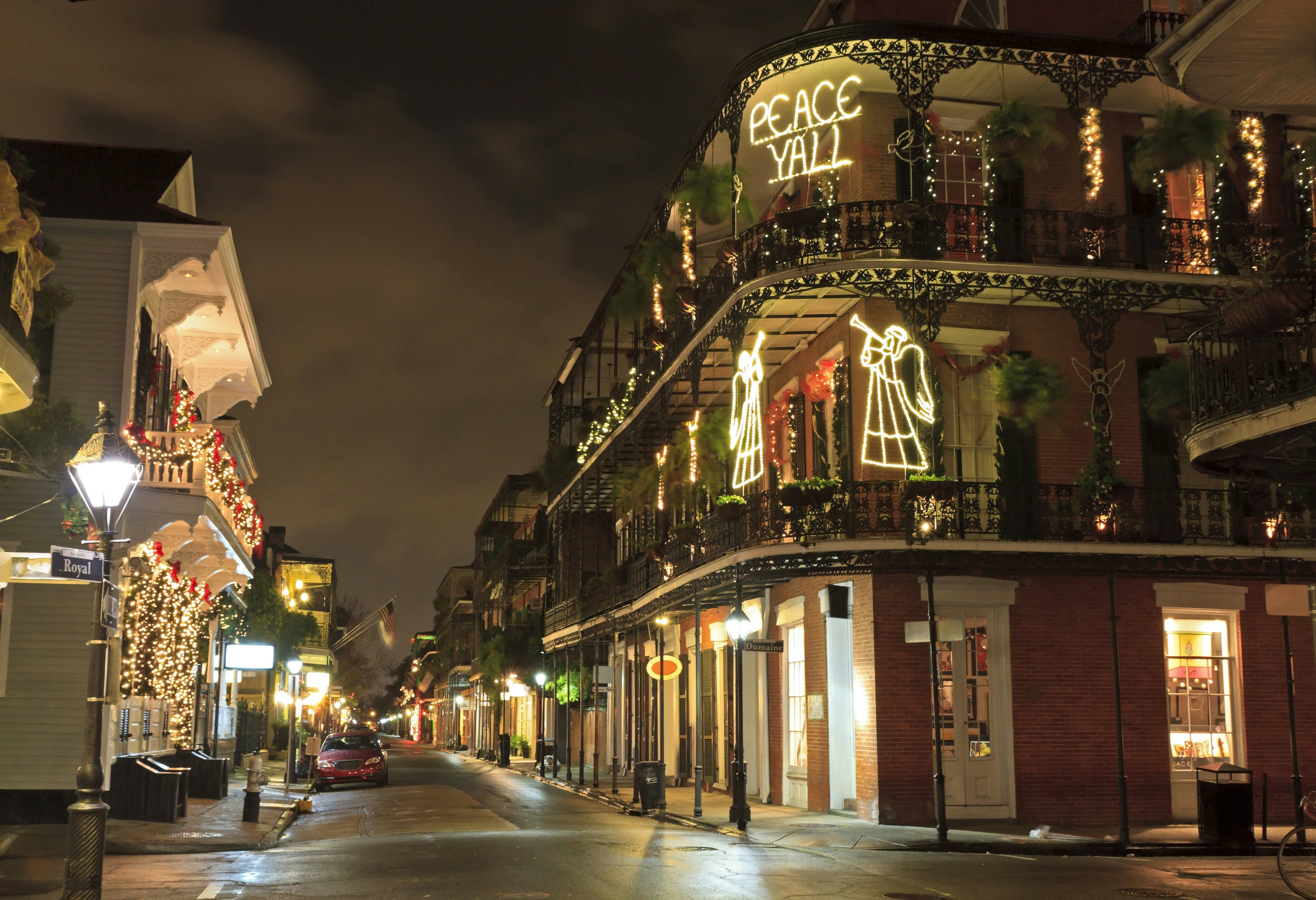 An empty city street. Buildings are lit up with Christmas decorations with one spelling out "peace y'all".