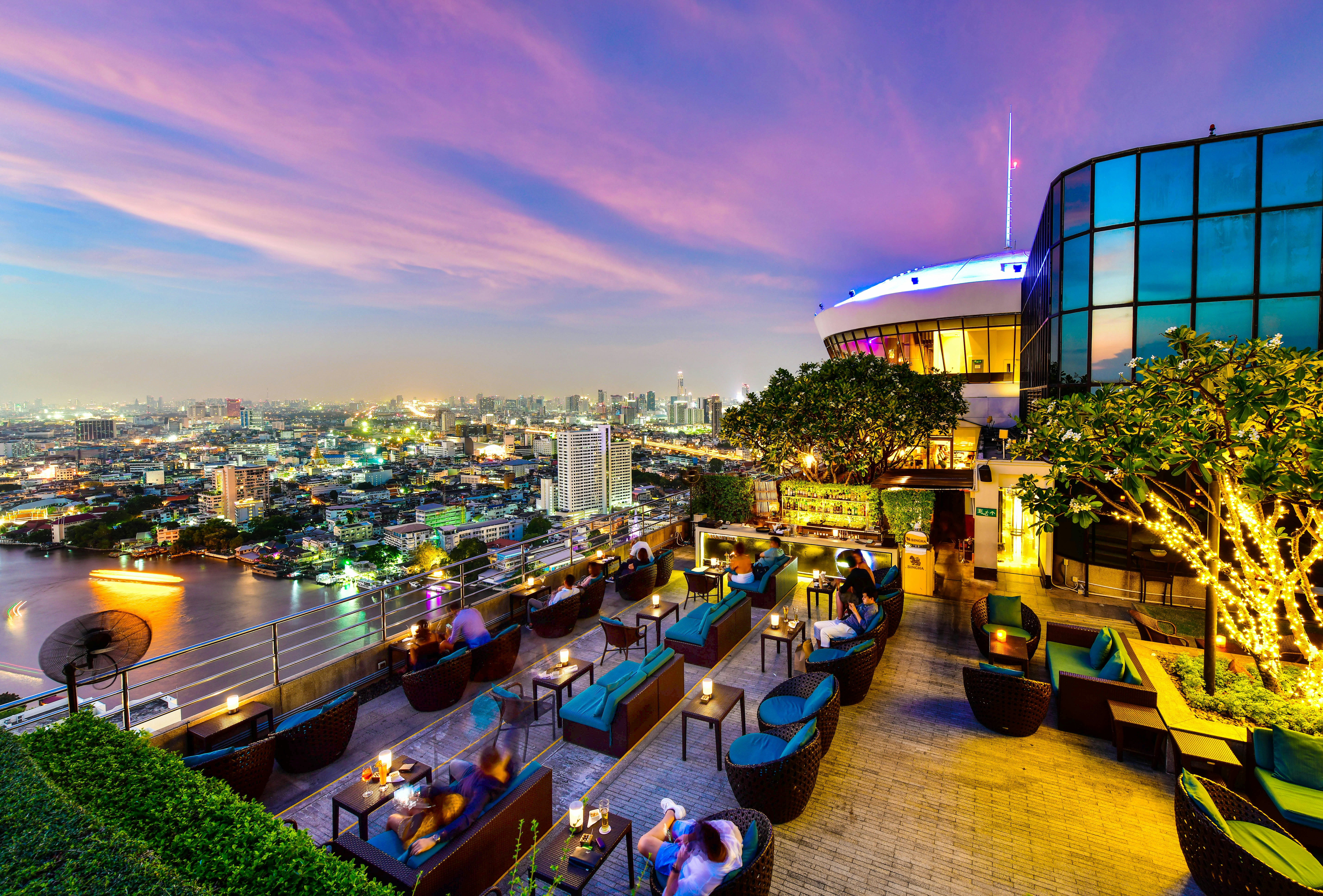 Diners and drinkers relaxing on lounge chairs on a rooftop restaurant with views over the river and city below.