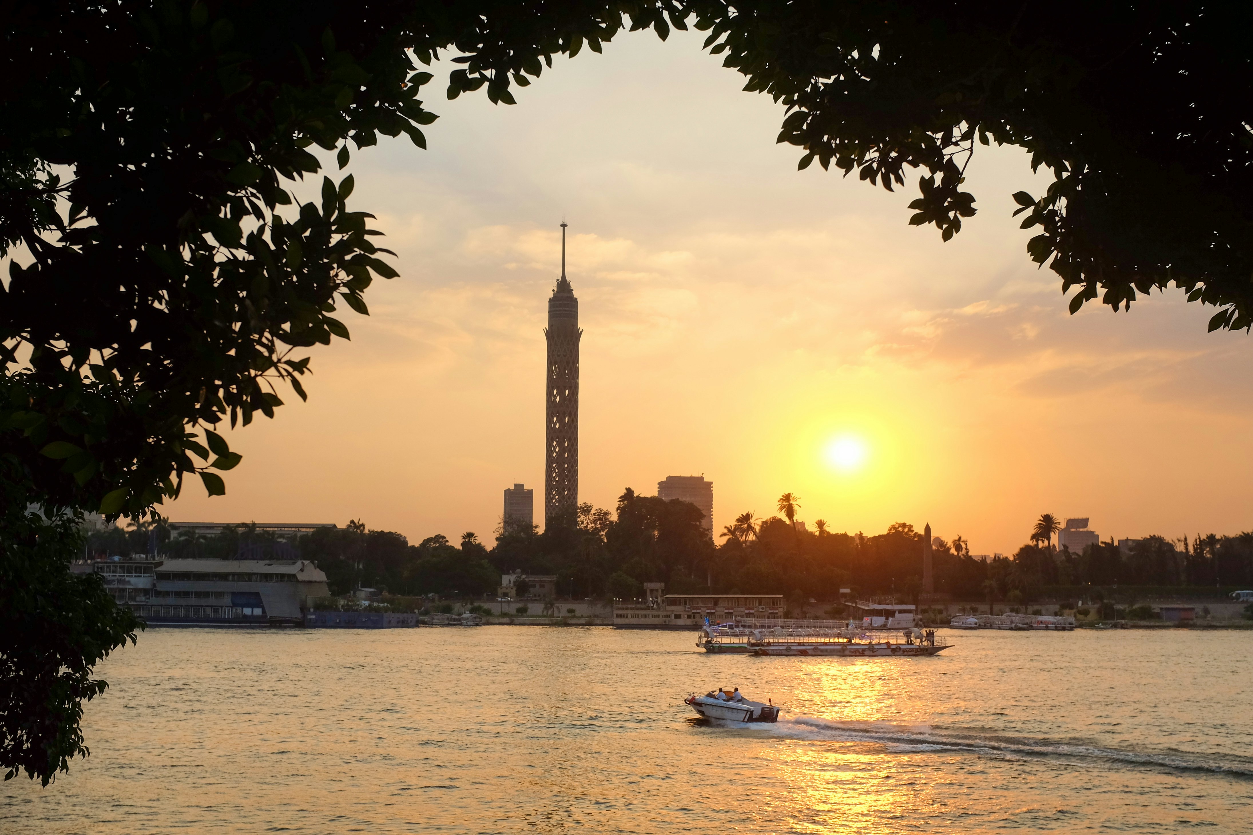 Boats on a river at sunset with a tall tower in silhouette on the shore.