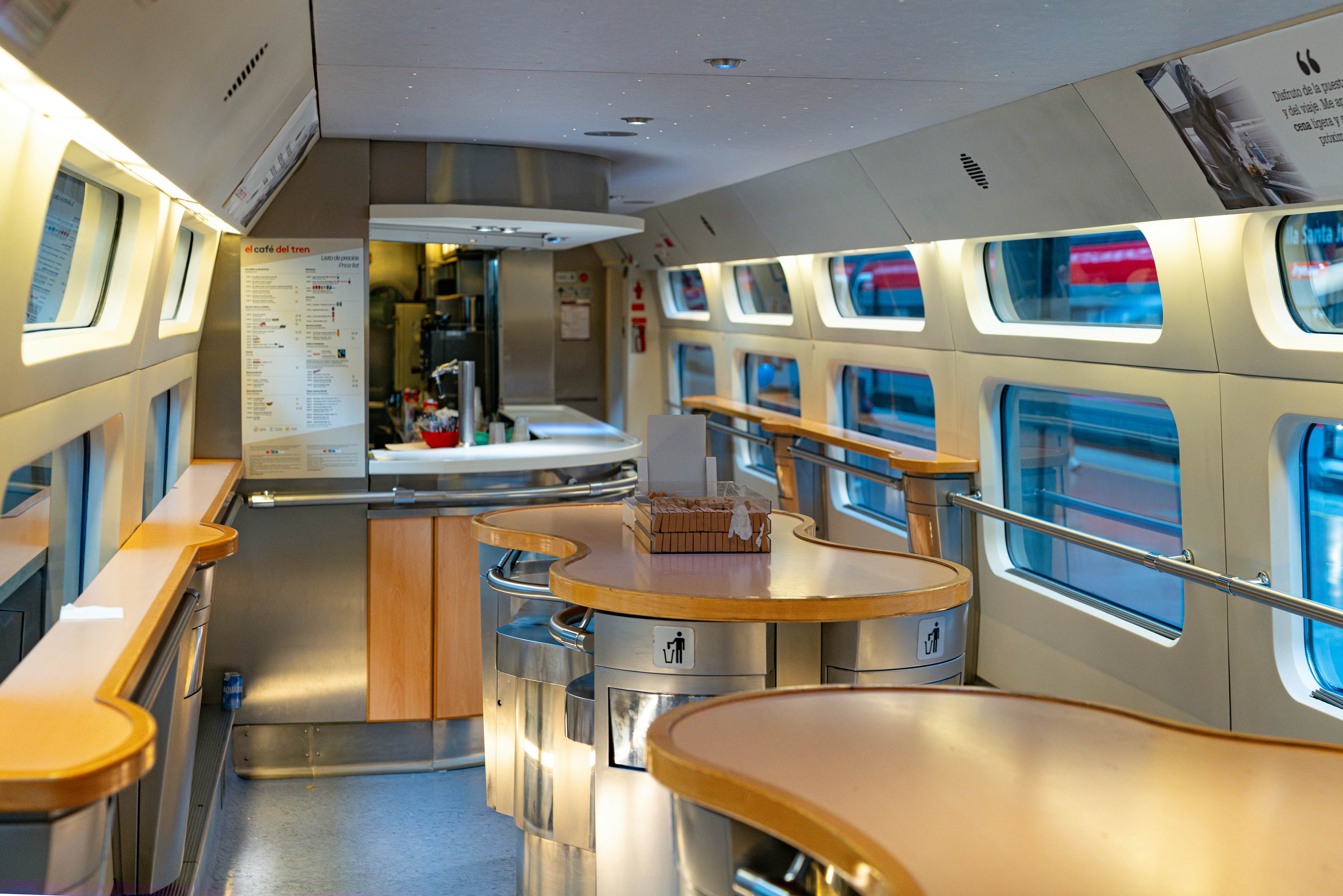 The interior of a train refreshments carriage with a counter for service and small tables for standing at.