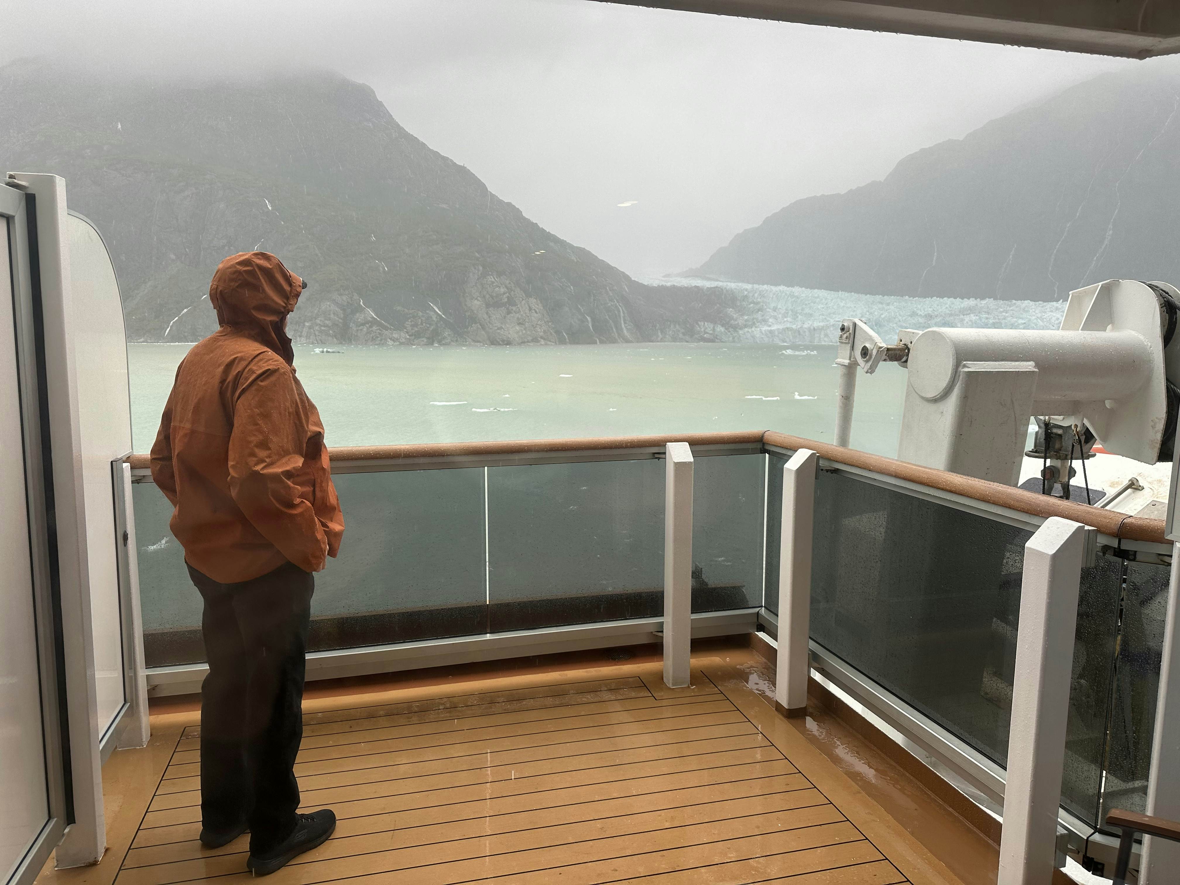A person on a ship balcony overlooking the sea on an overcast day.