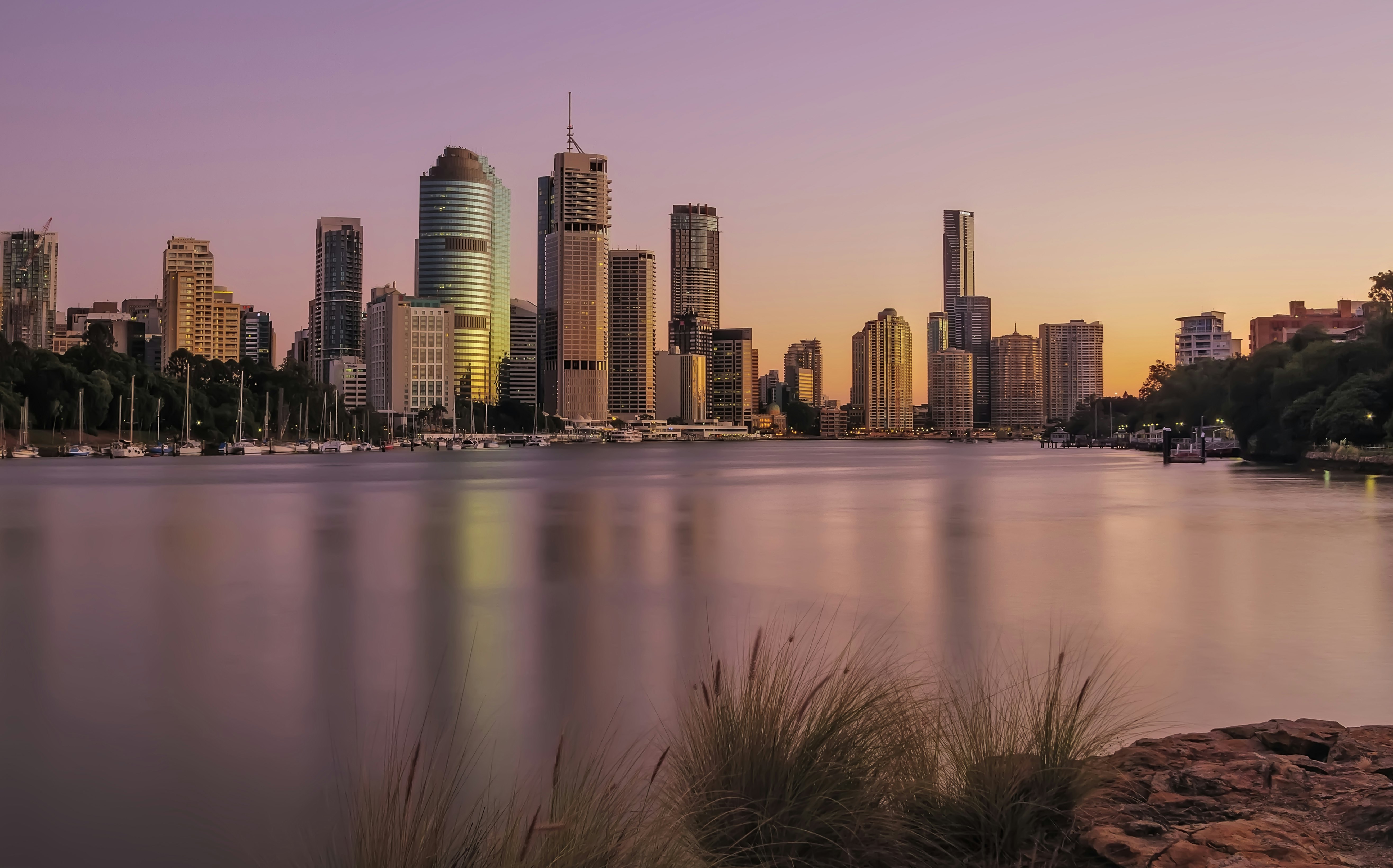 City skyline at sunrise with pinkish hue on water in the foreground.