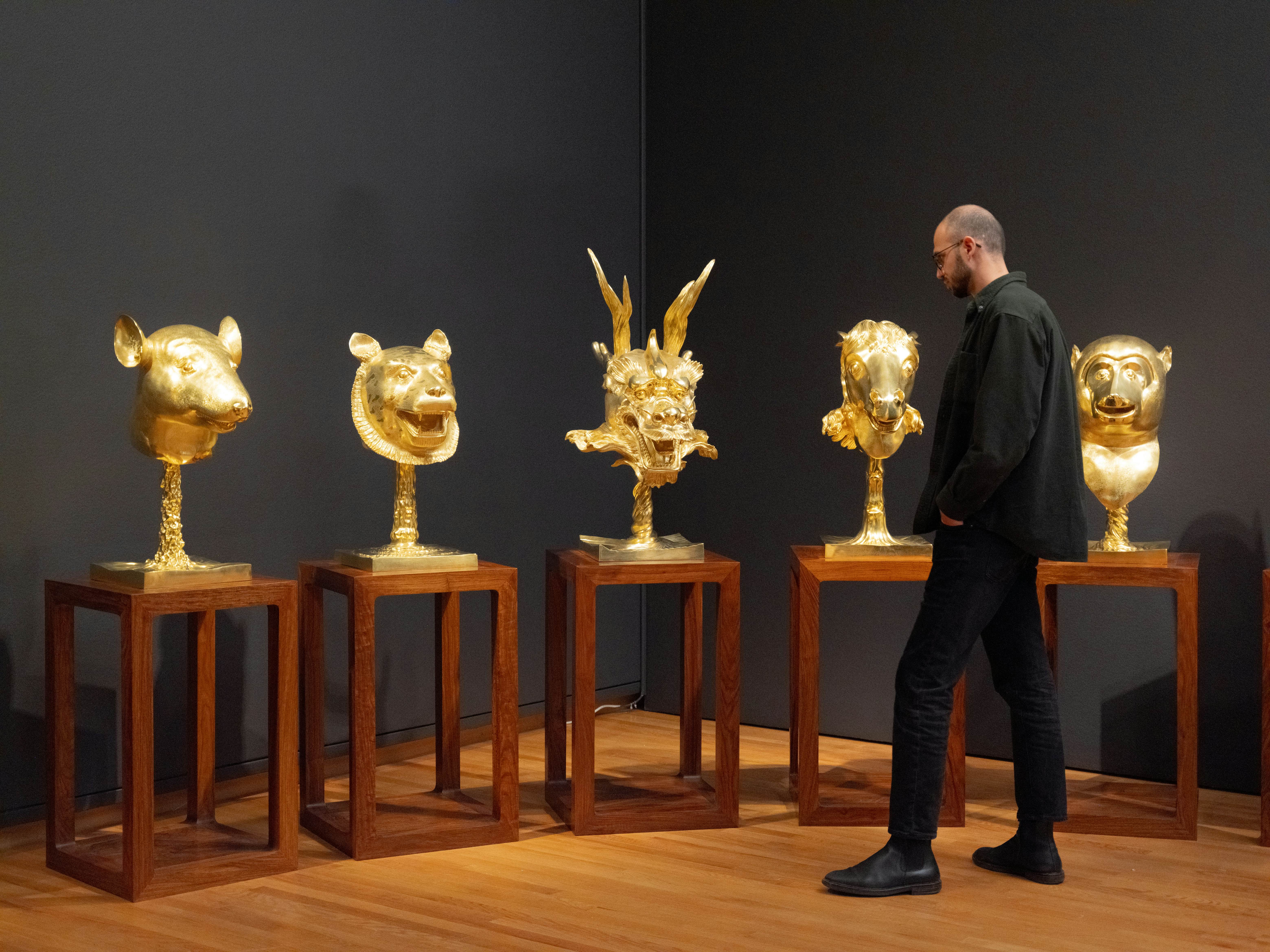A man looks at gold-covered sculptures in a museum gallery.