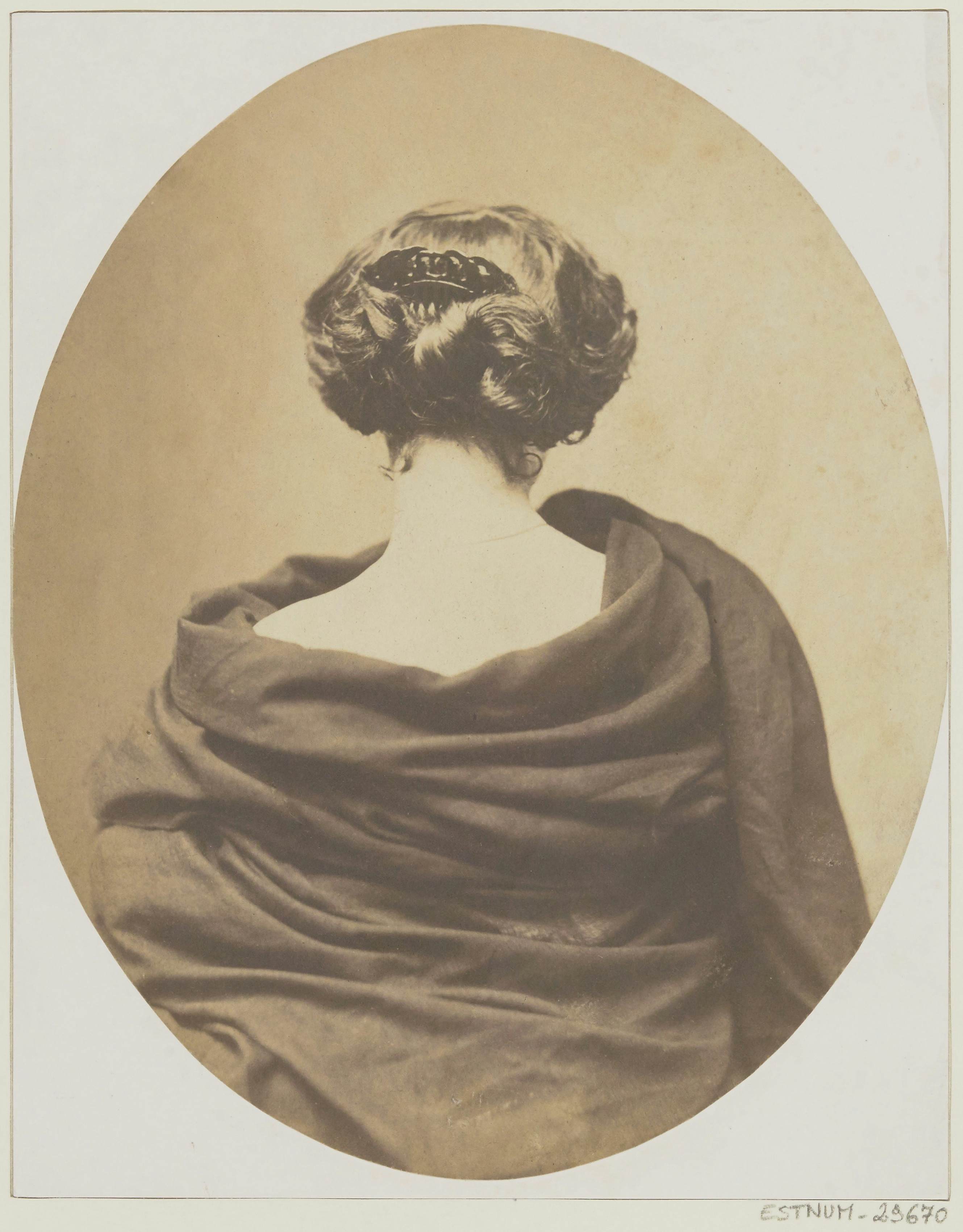 An antique photograph shows the back of a woman draped in stylish fabric.