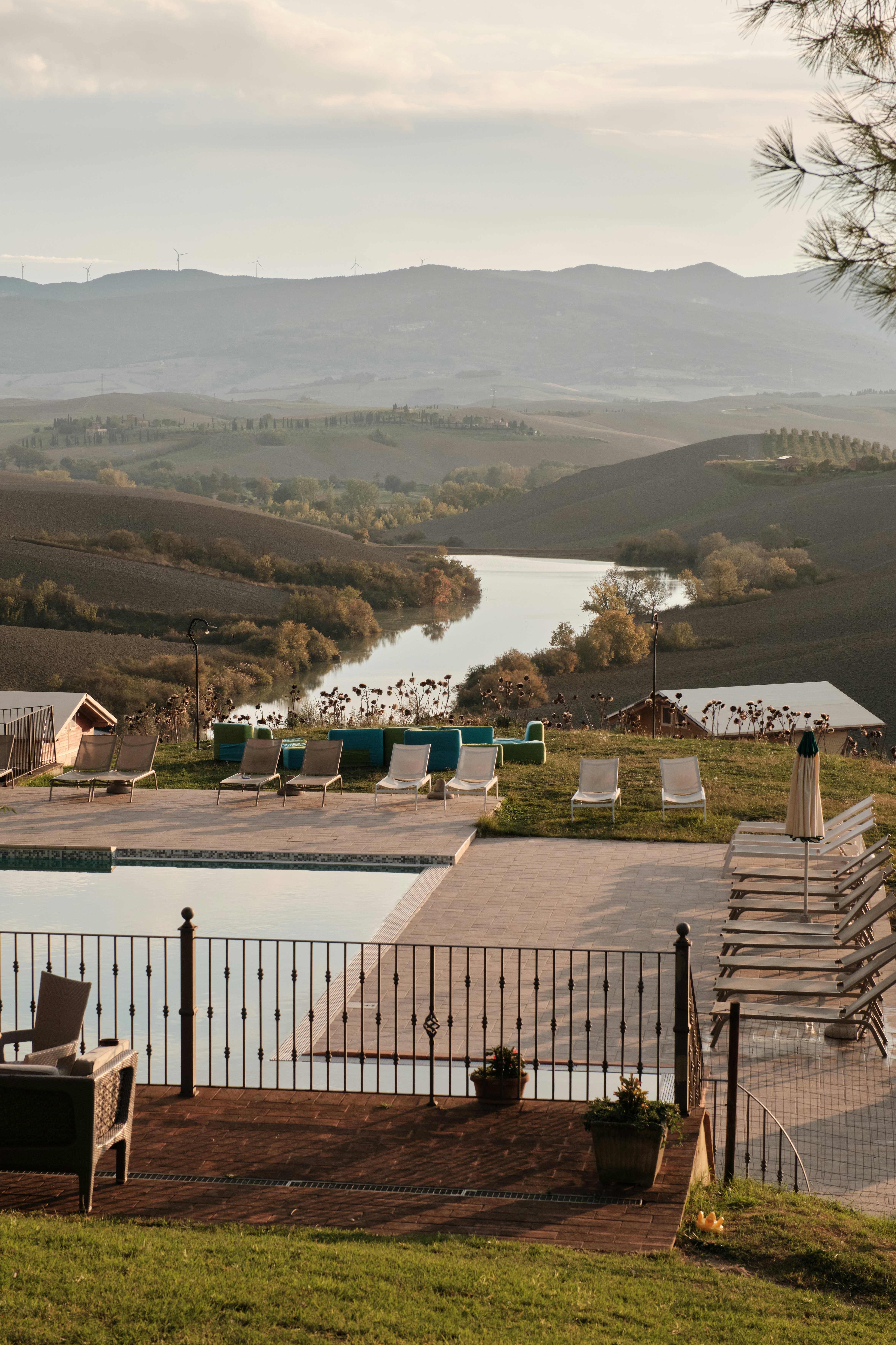 Sunloungers surround a small rectangular pool in a rural region with a river and rolling hills.