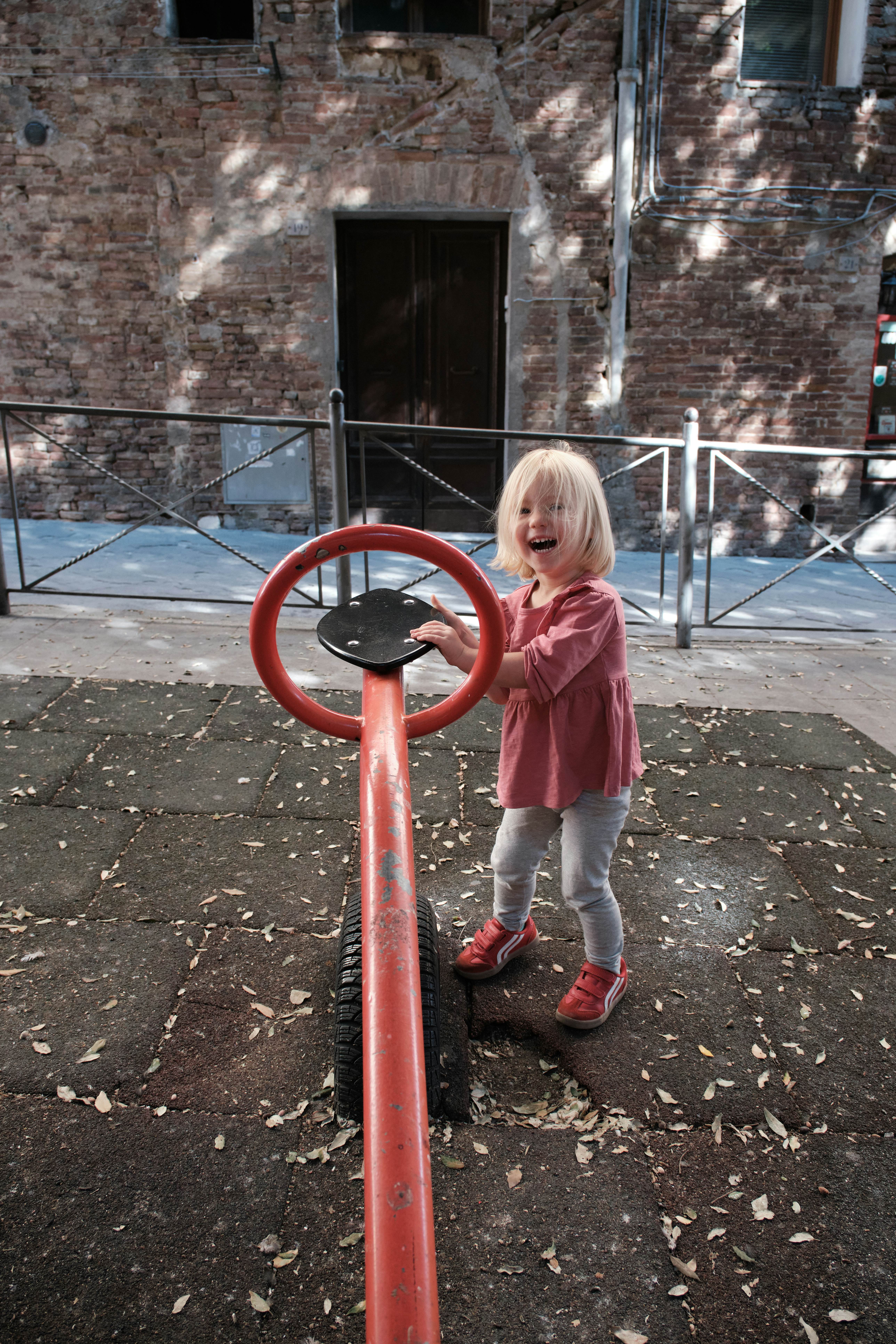 A child playing with one side of a see-saw in a city playground.