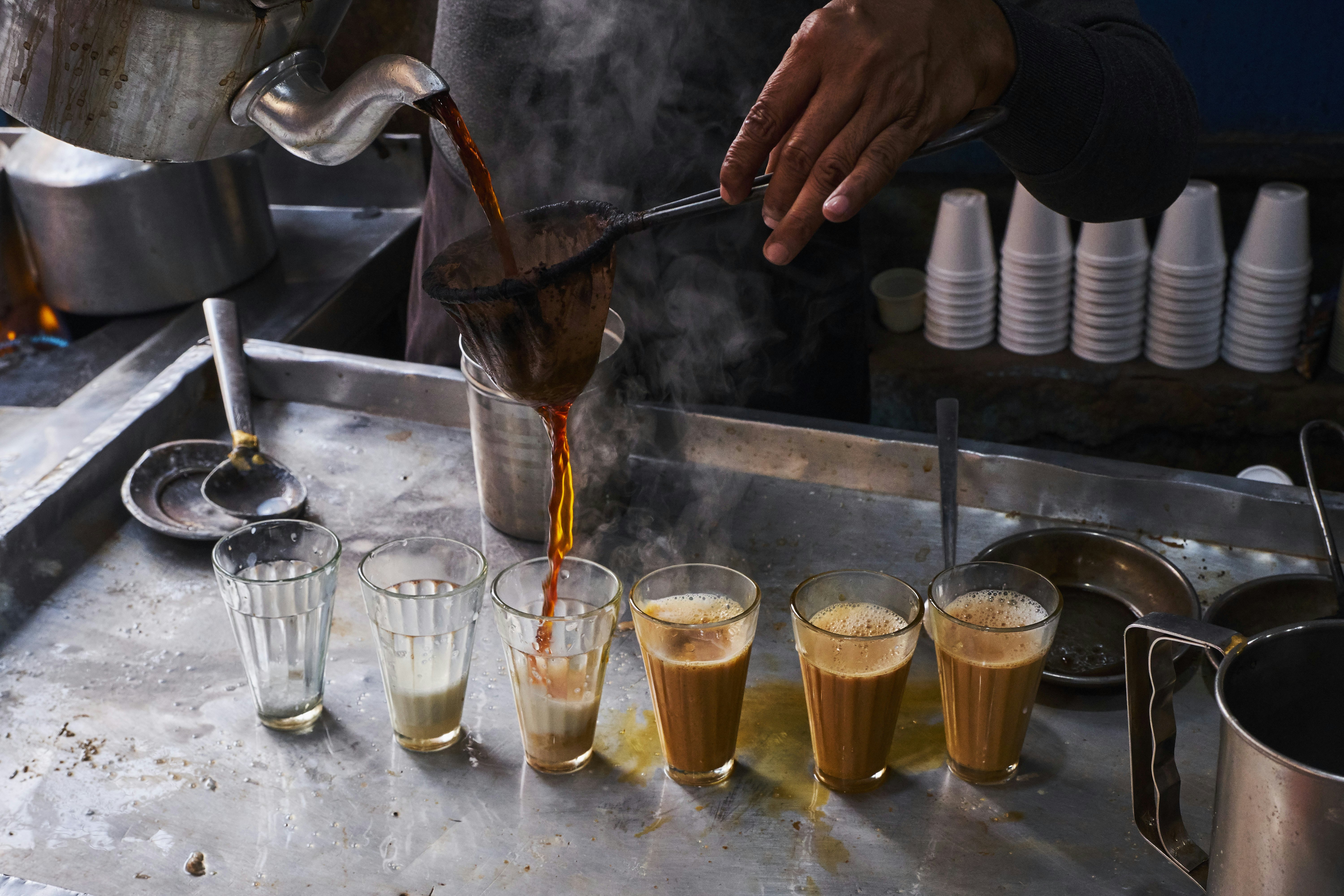 Tea is poured into a row of glass tumblers on a metal counter.