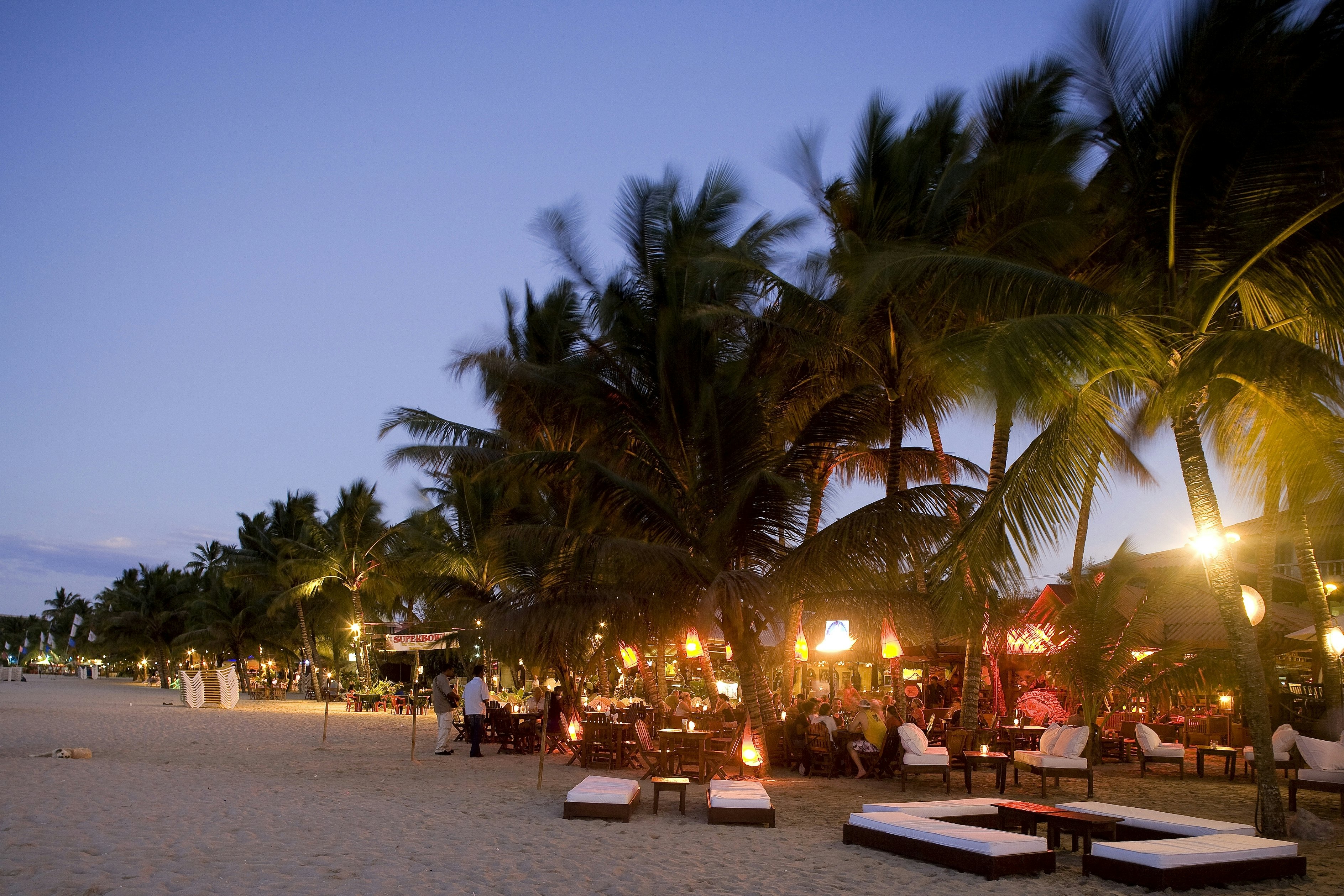 People sit at tables under glowing lights at a beach bar in the Dominican Republic.
