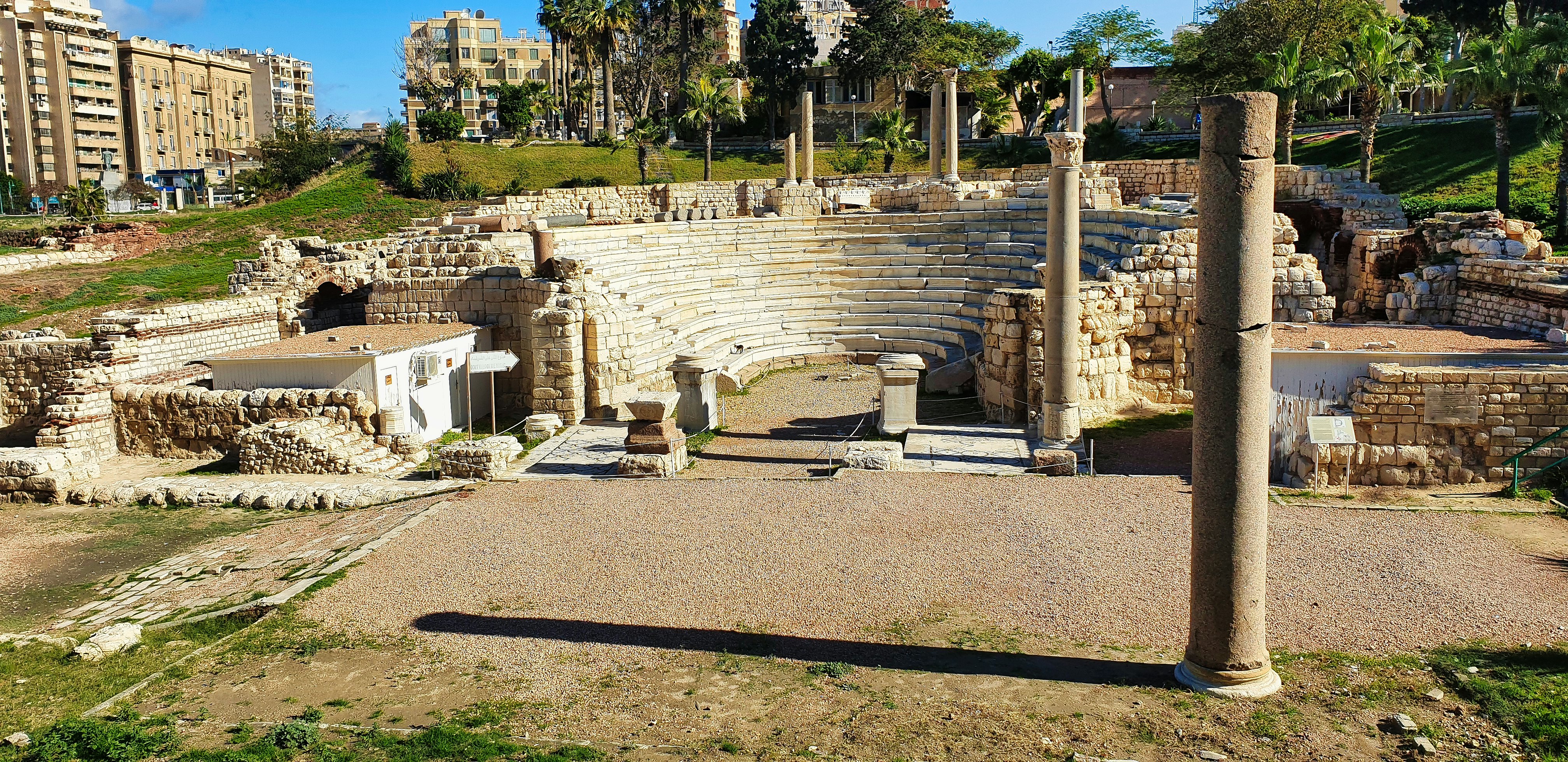 A Roman amphitheater set into a hillside in a park in Egypt; several tall columns are around the site.