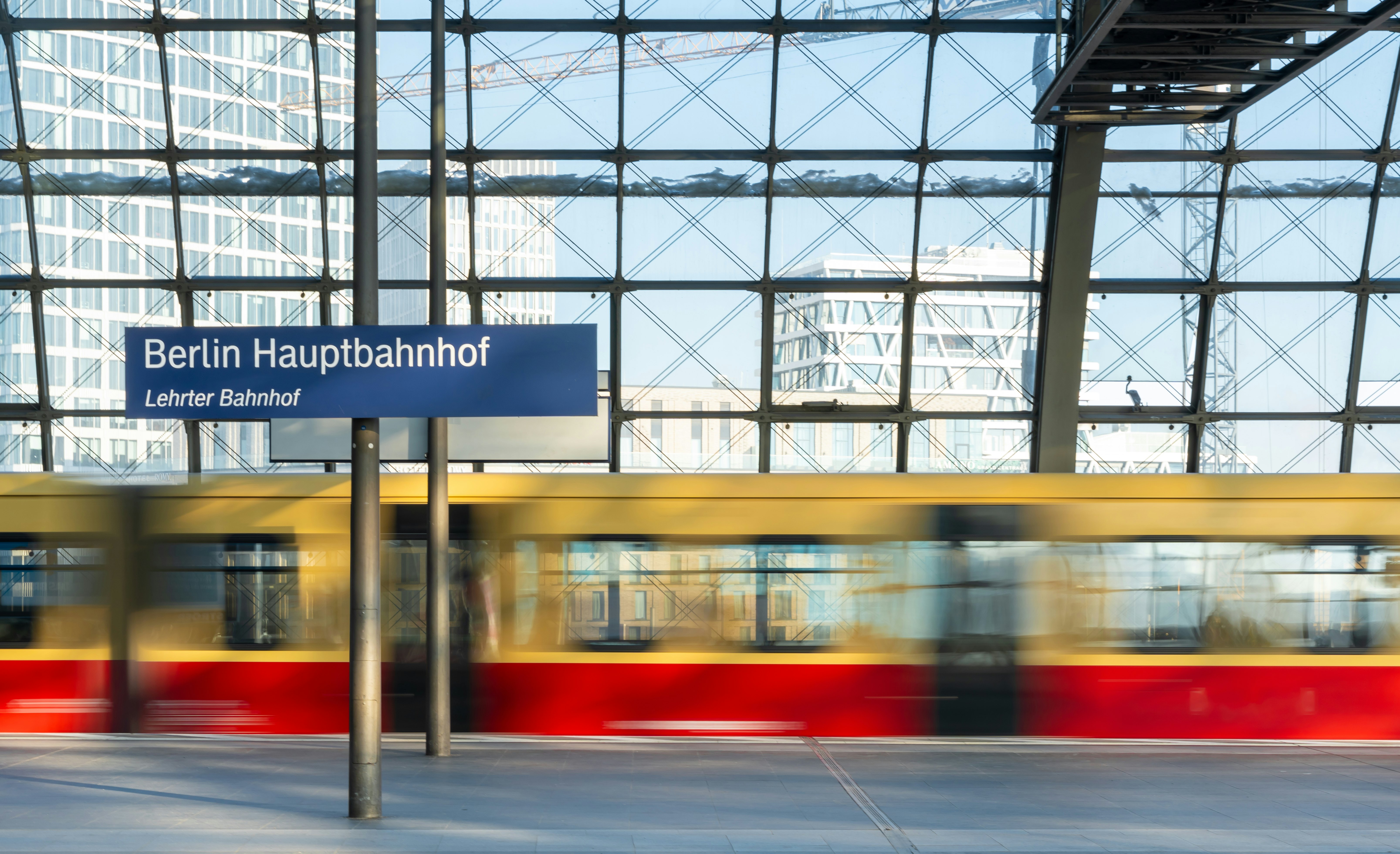 A yellow and red train passes through a station as a blur.