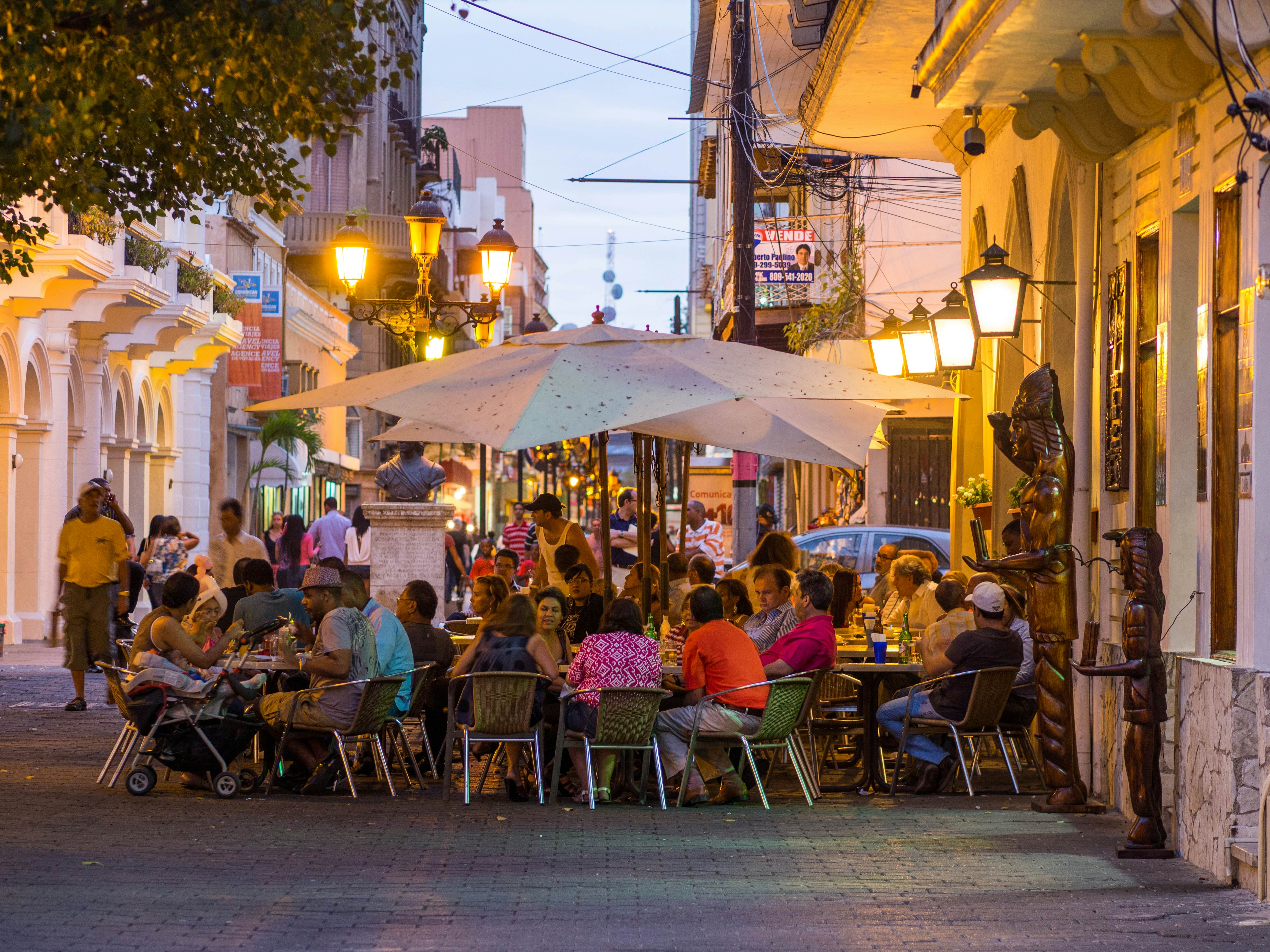 People sit at a sidewalk cafe under umbrellas at dusk in a historic part of town in the Dominican Republic.
