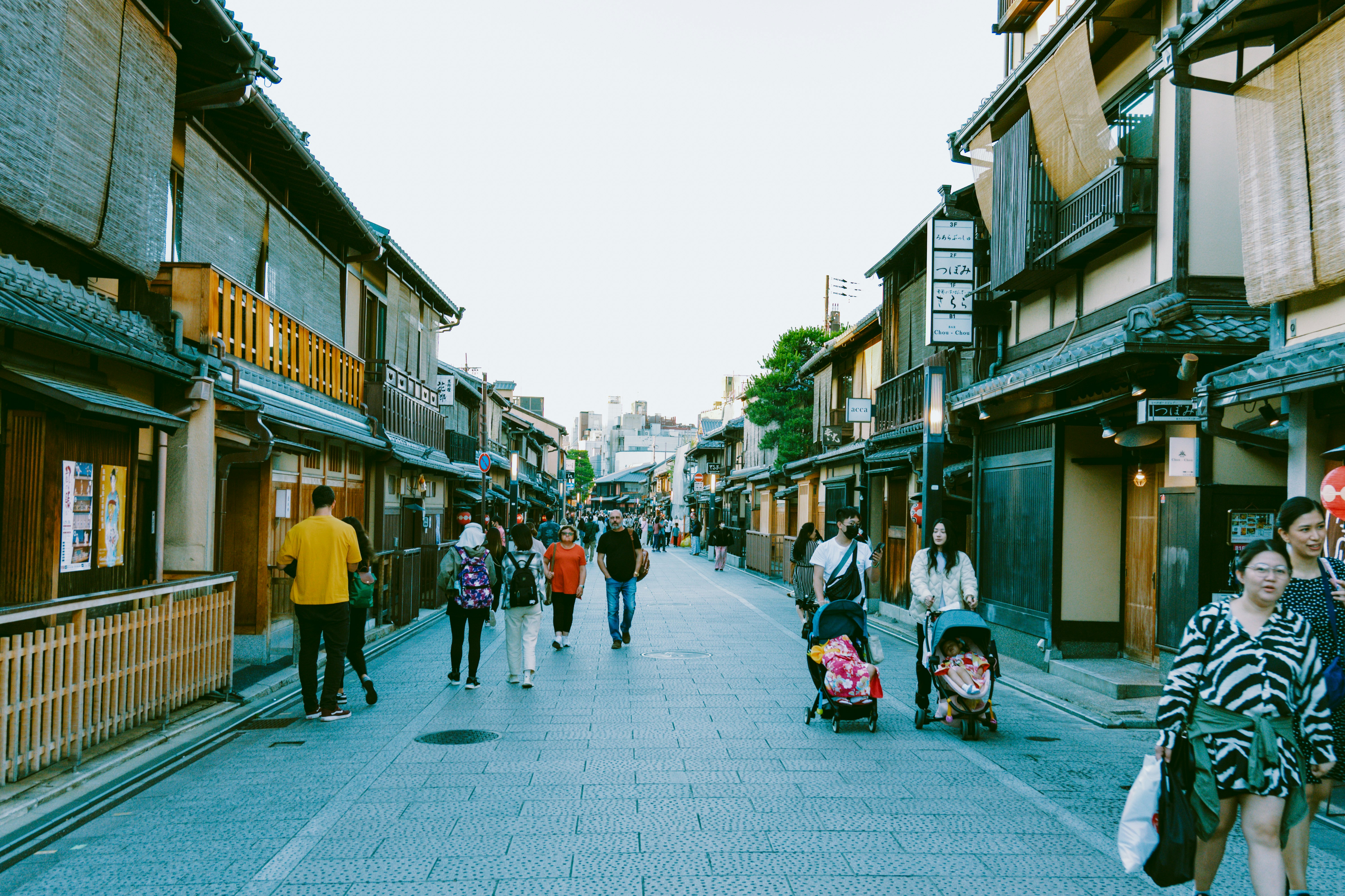 Pedestrials wander through a street in Japan. Two people are pushing strollers with toddlers in them.